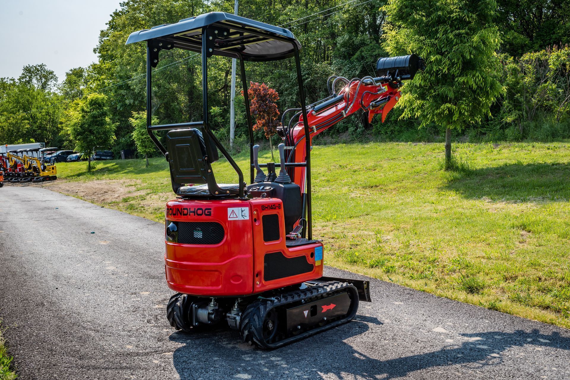 A small, bright red tracked excavator with a canopy, parked on a gravel path outdoors near grass and trees.