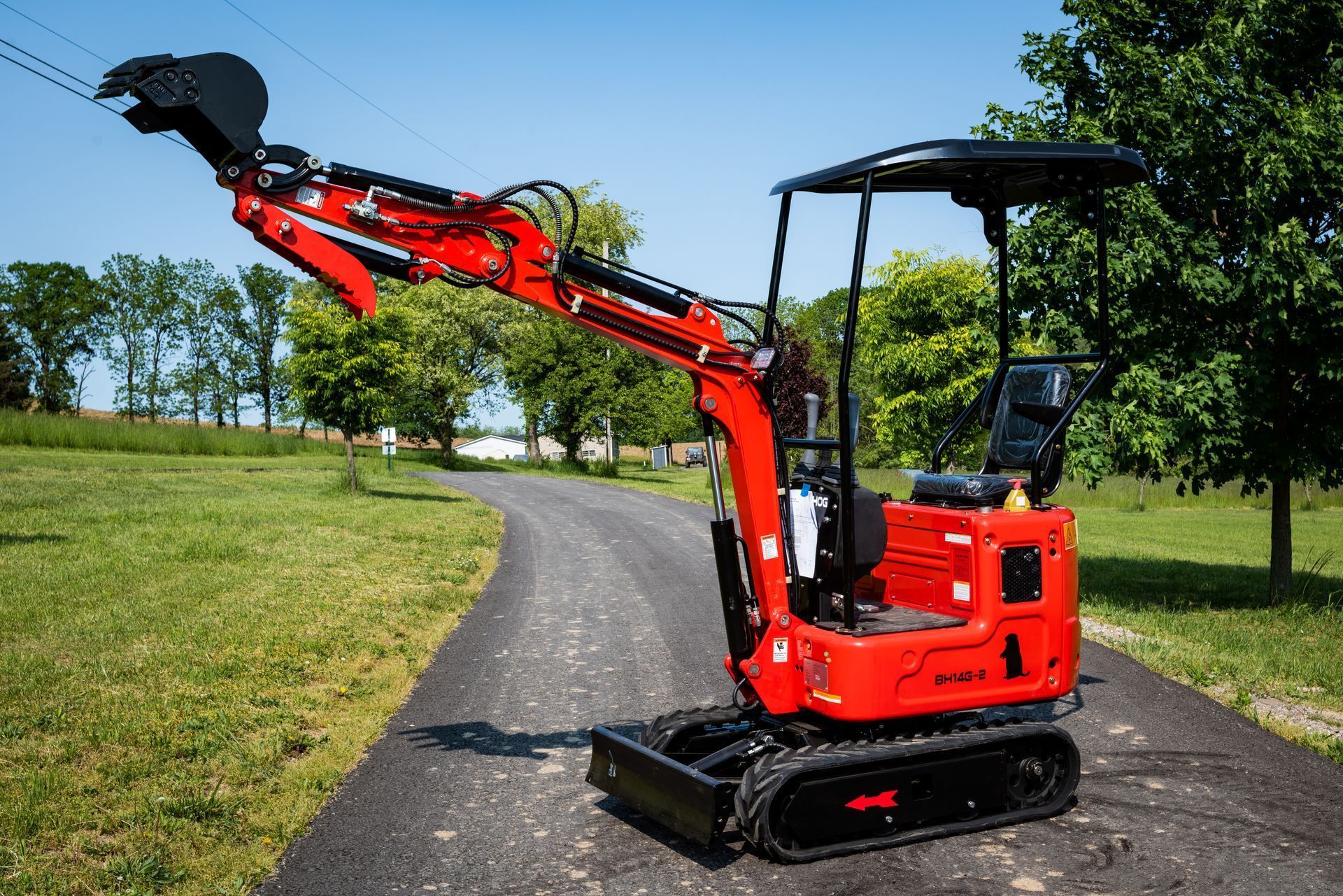 A bright red compact excavator parked on a paved path in a grassy field on a sunny day.