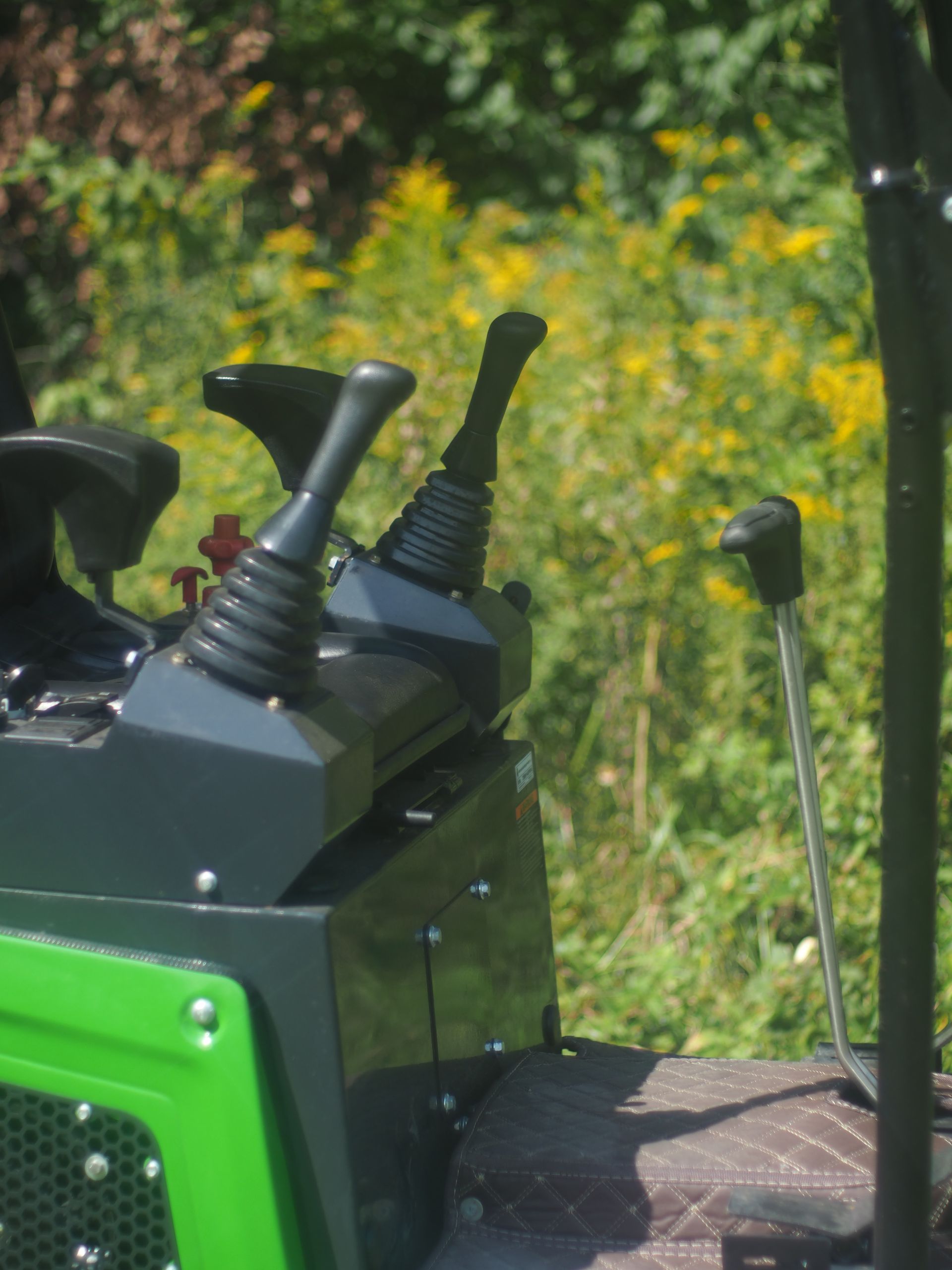 Close-up of control levers on a green piece of outdoor machinery, with greenery visible in the blurred background.