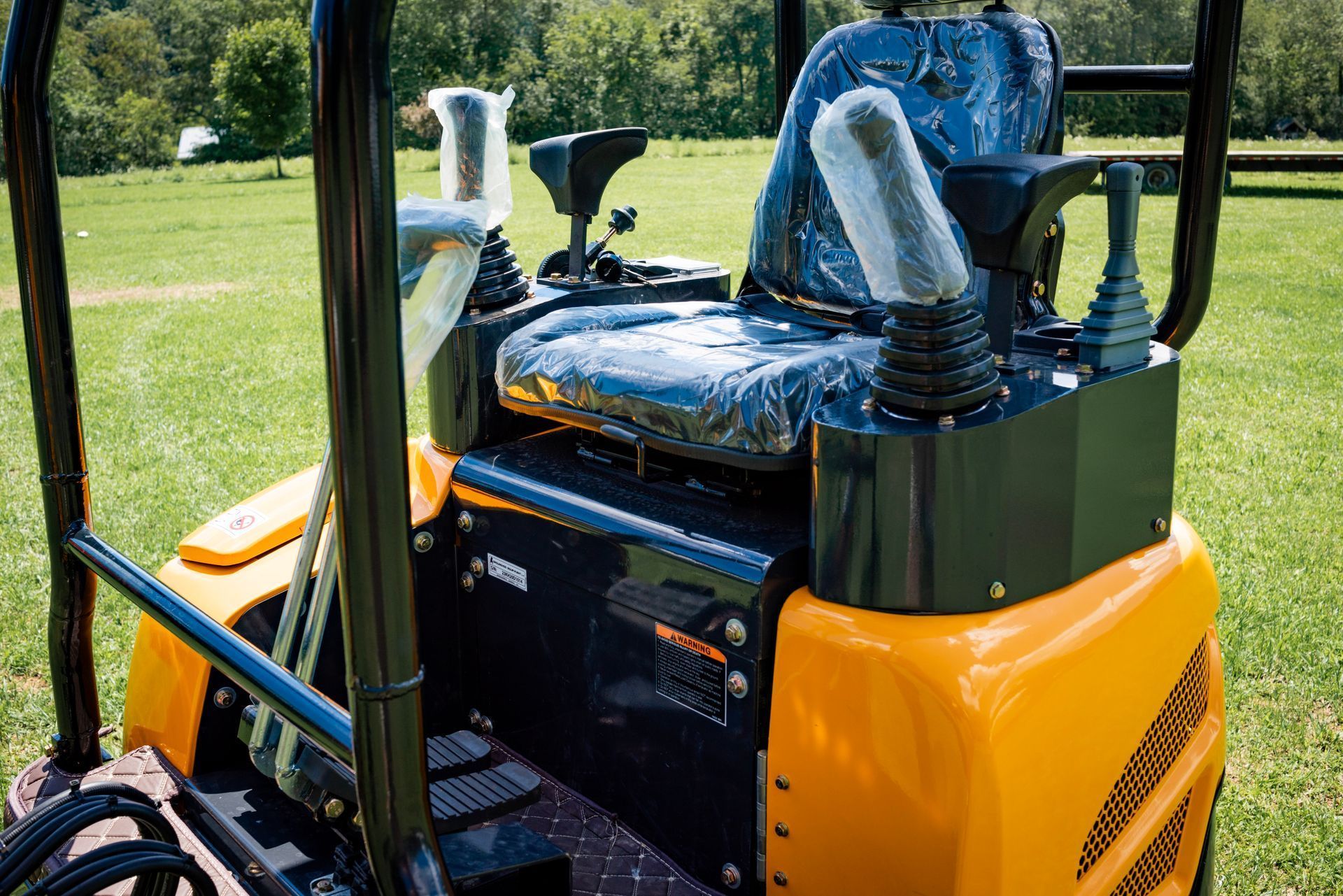 The seat and control levers of a yellow mini-excavator parked in a grassy field.