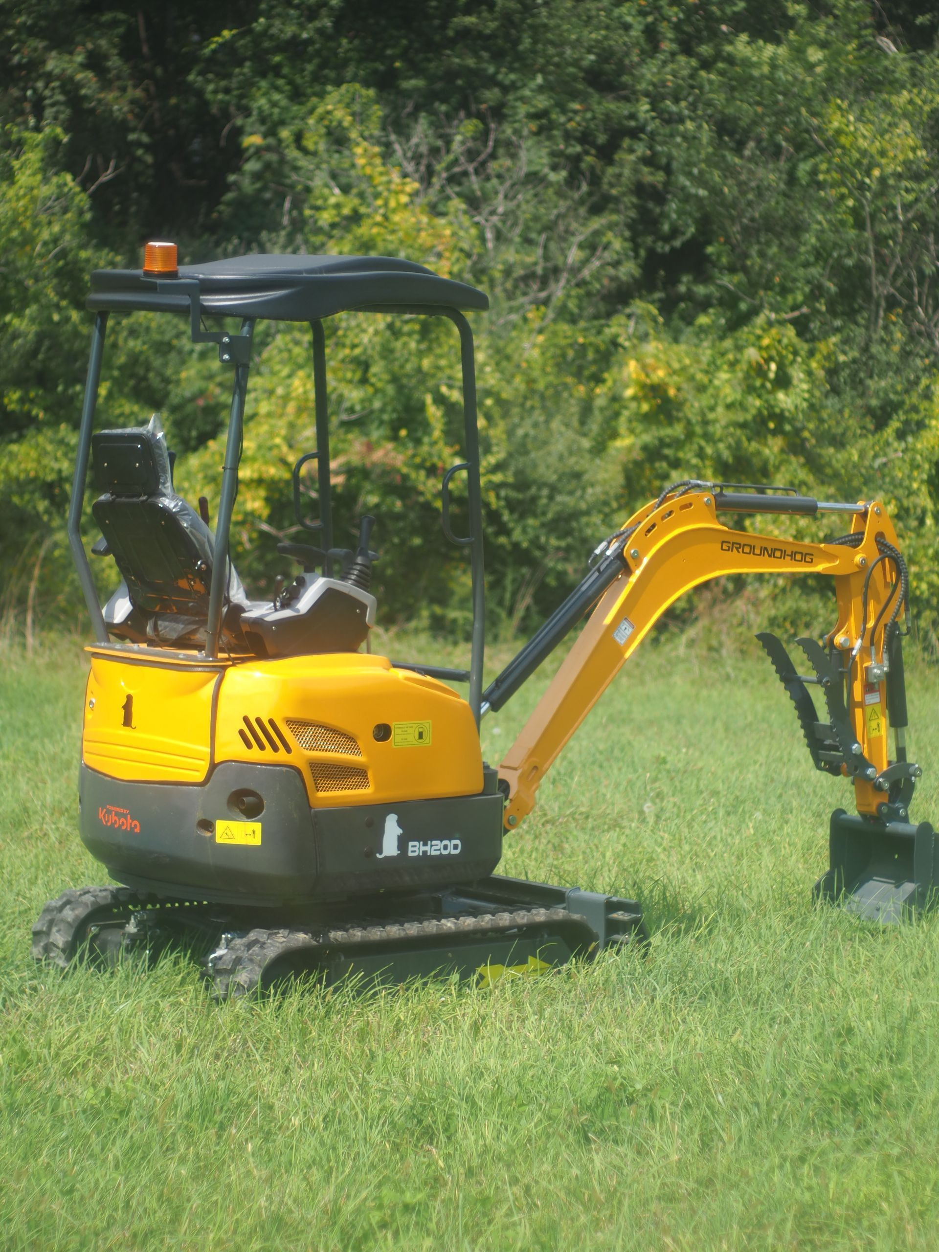 A yellow and gray mini excavator sits on a grassy field with trees in the background.