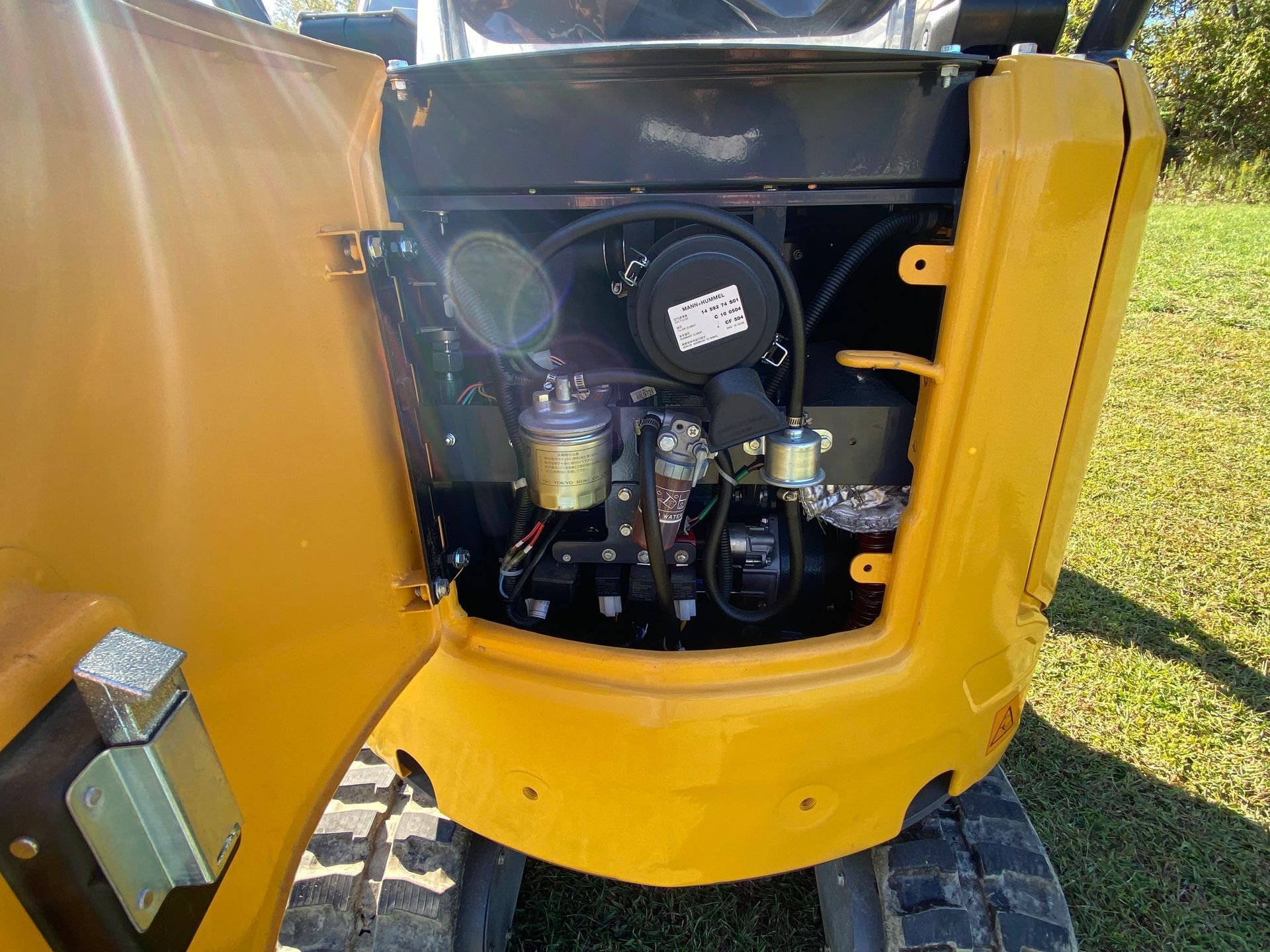 An open engine compartment on a yellow mini excavator, showing internal components like the fuel filter and air cleaner.