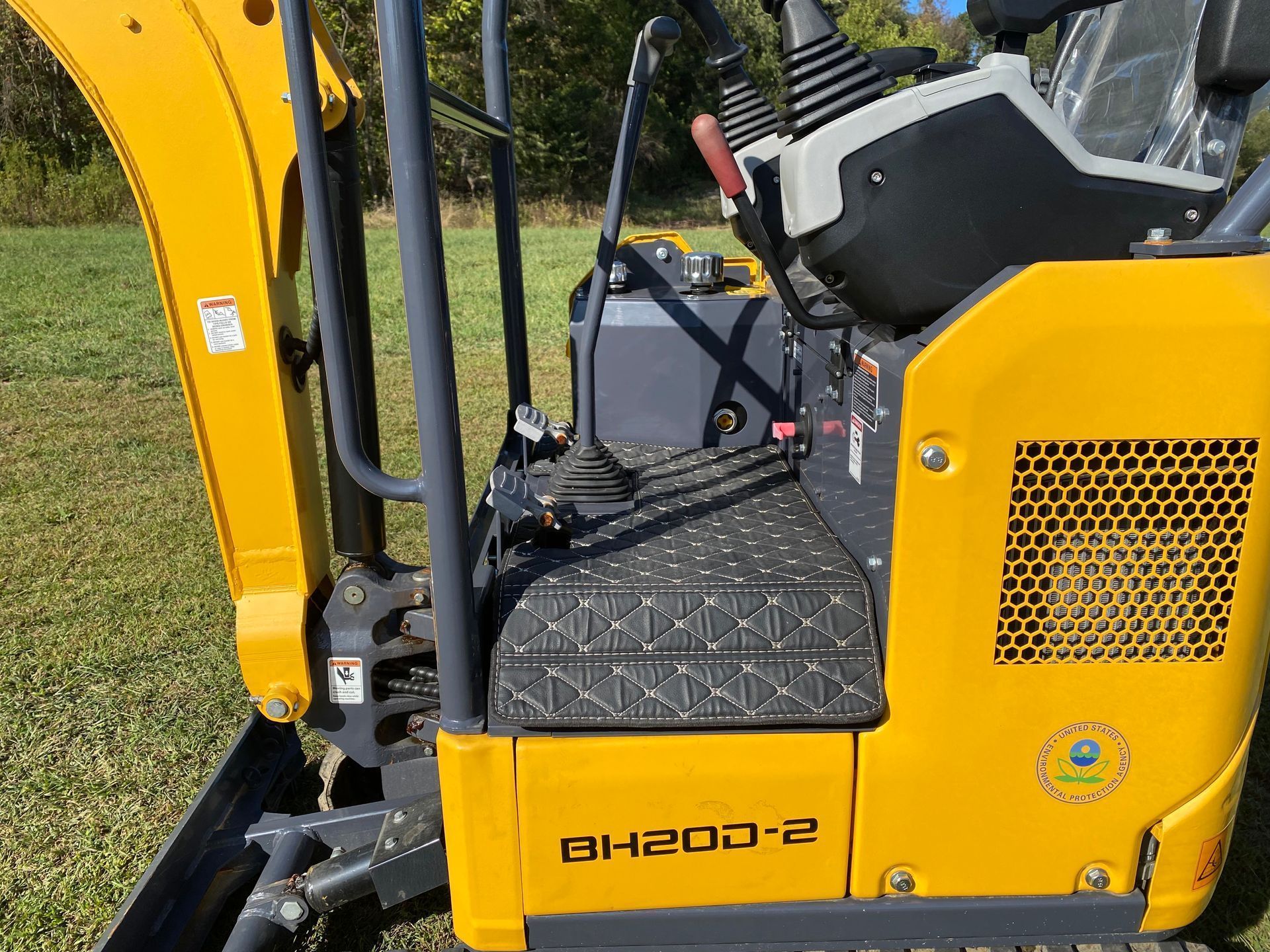 Close-up side view of the operator station of a yellow BH200-2 mini excavator, showing controls and floor matting.