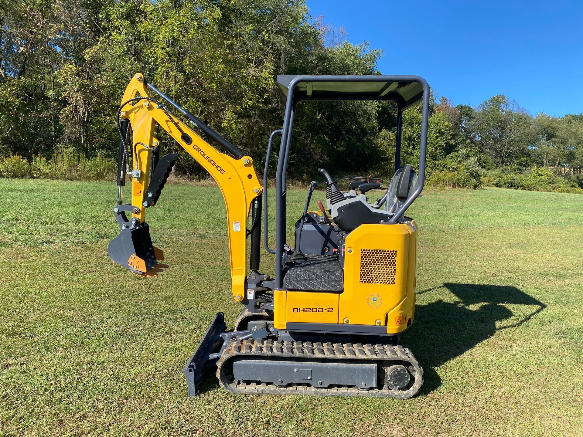 A bright yellow mini excavator sits on a grassy field under a clear blue sky.