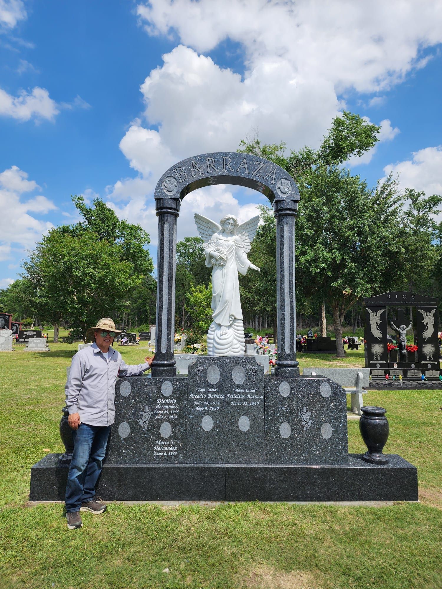 A man is standing in front of a large statue of an angel in a cemetery.