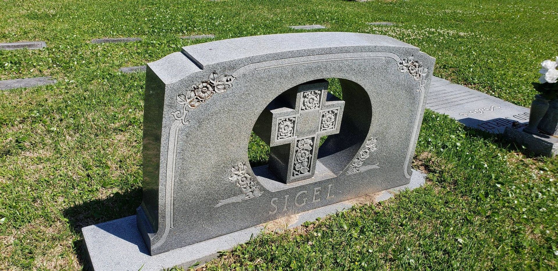 A gravestone with a cross in the middle of it in a cemetery.