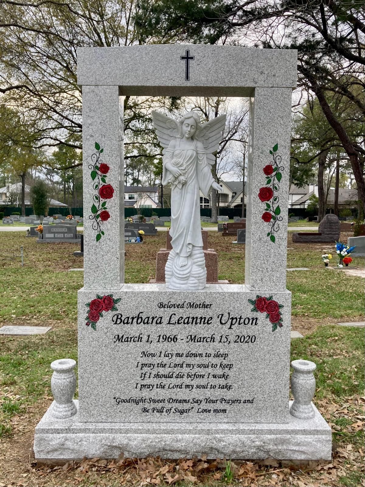A gravestone with a statue of an angel and roses in a cemetery.