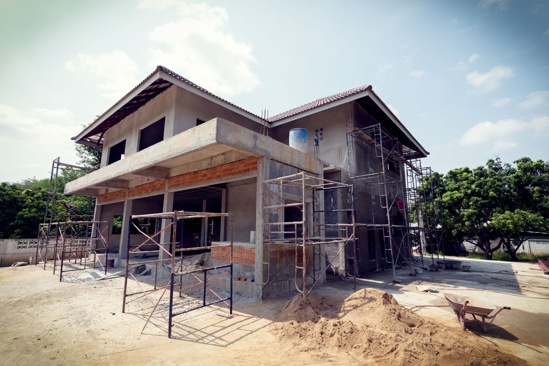 Two-story house under construction; scaffolding, concrete, and exposed brick; bright sunny day.