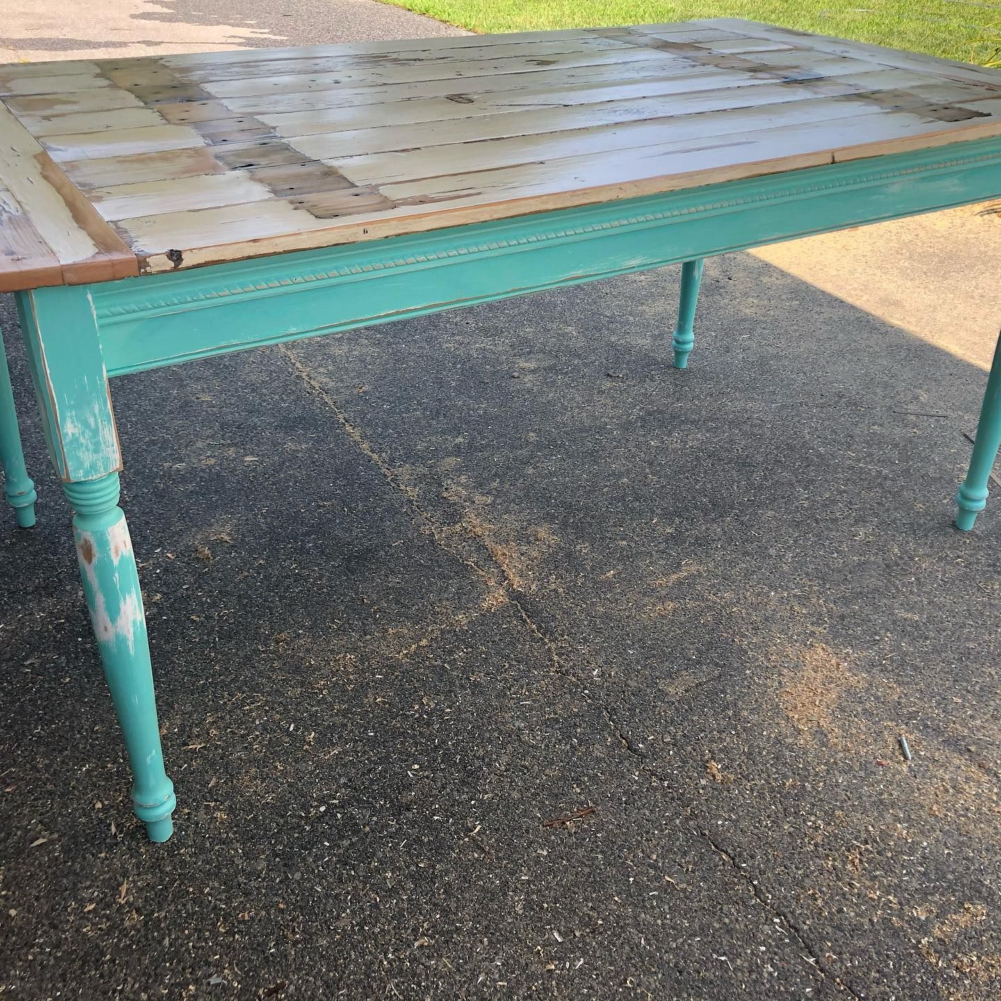 Aqua-painted wooden table with a light-colored, aged tabletop, sitting on a paved surface.