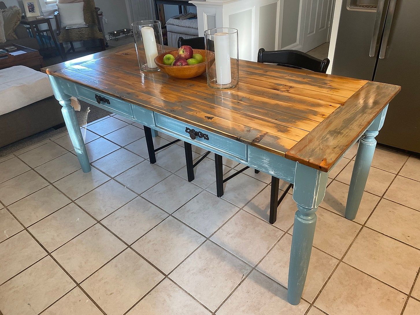 Wooden dining table with blue legs, brown top, and a bowl of apples in a home setting.