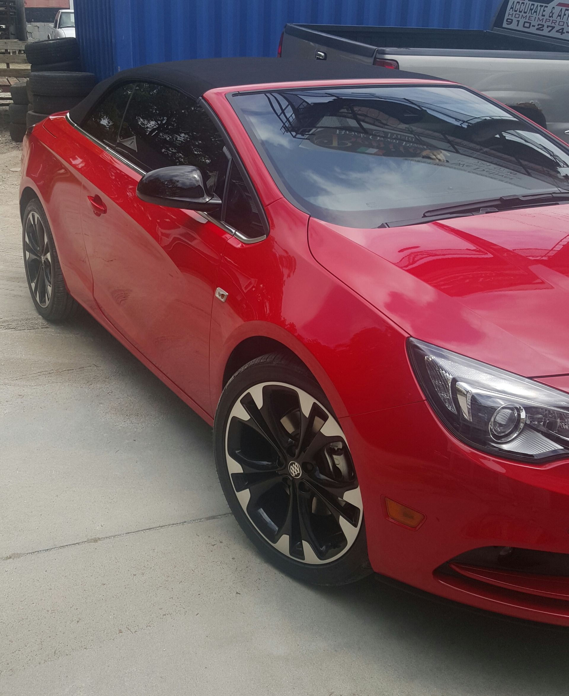 A red convertible car is parked in front of a blue container