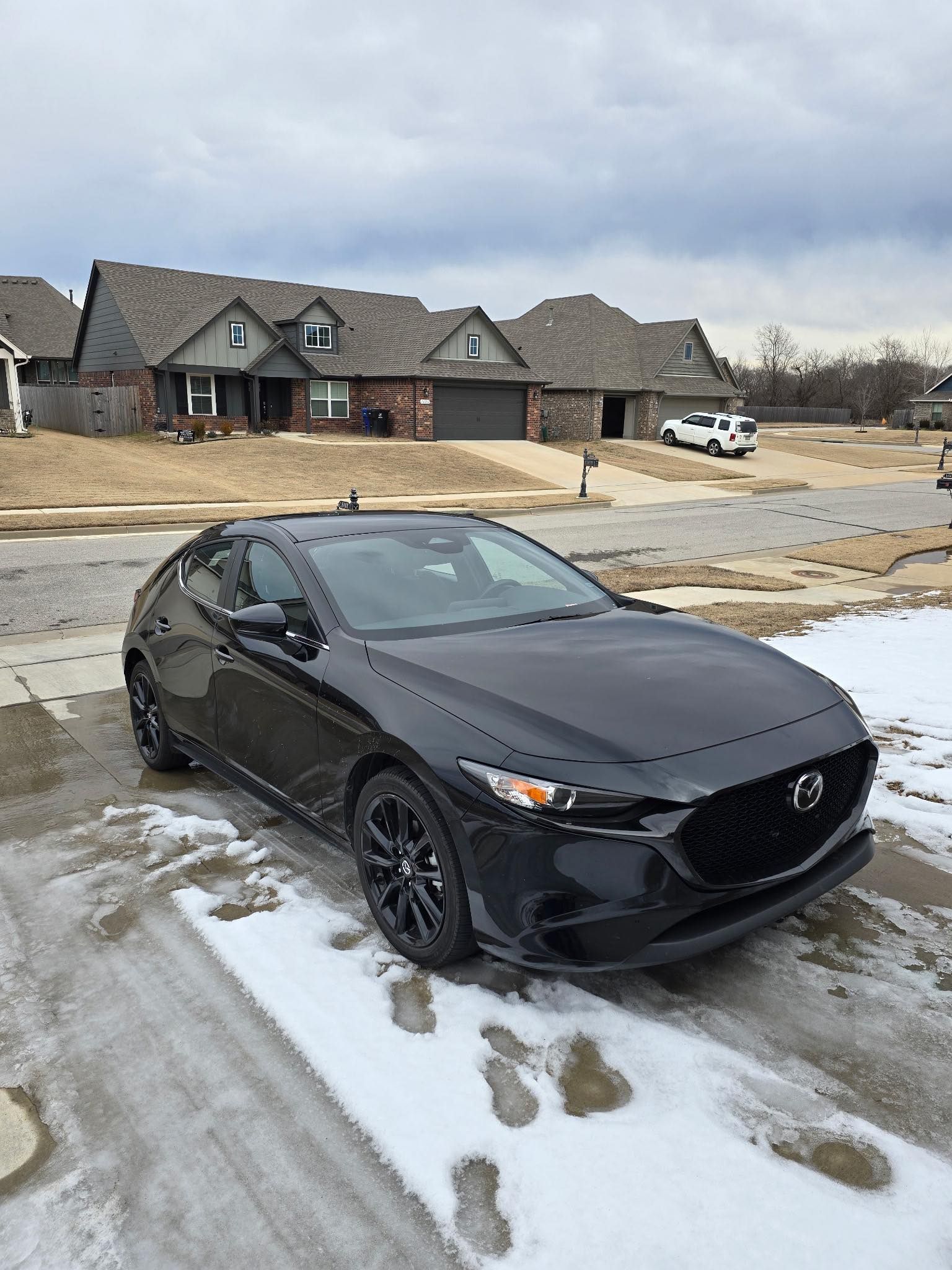 A black car is parked in the snow in front of a house.