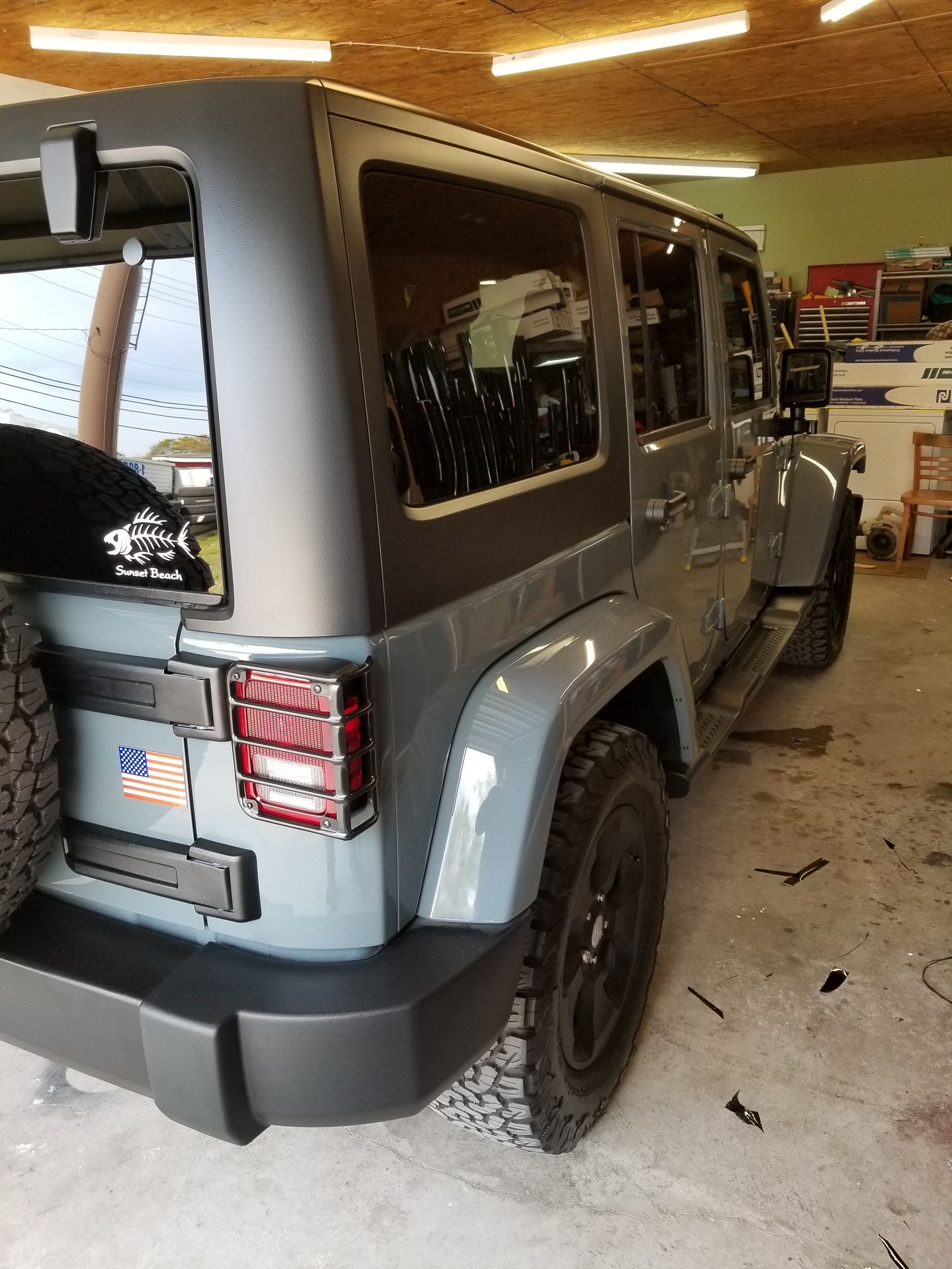 A jeep is parked in a garage with a tire on the back.