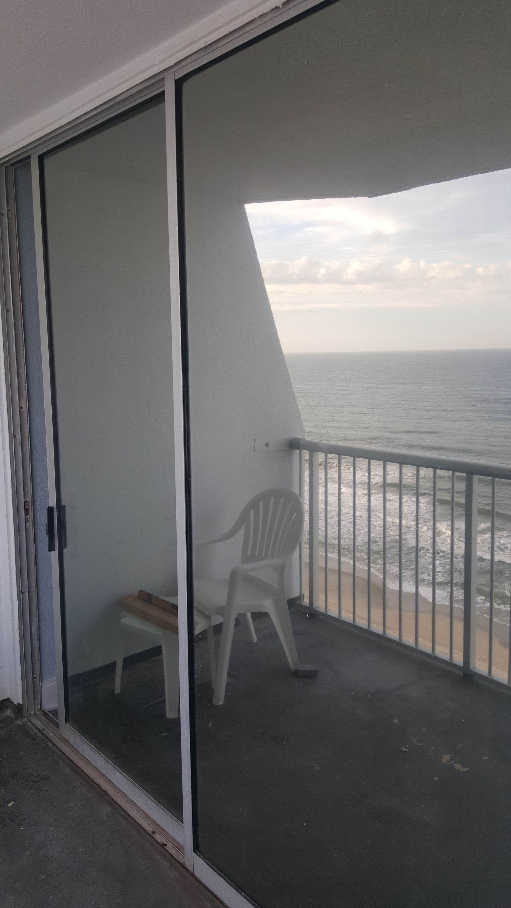 A balcony with a chair and a table overlooking the ocean.