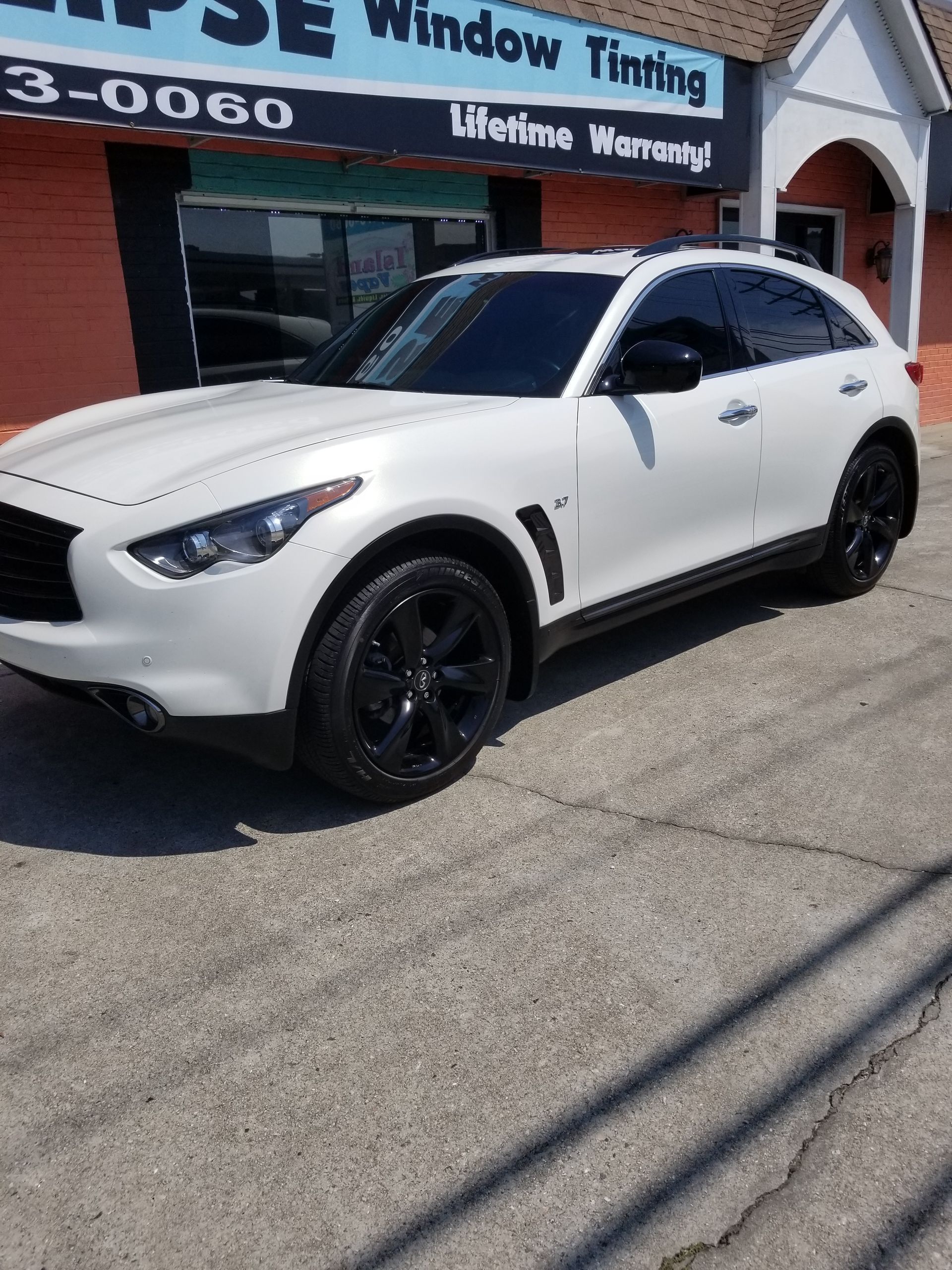 A white car is parked in front of a window tinting shop.