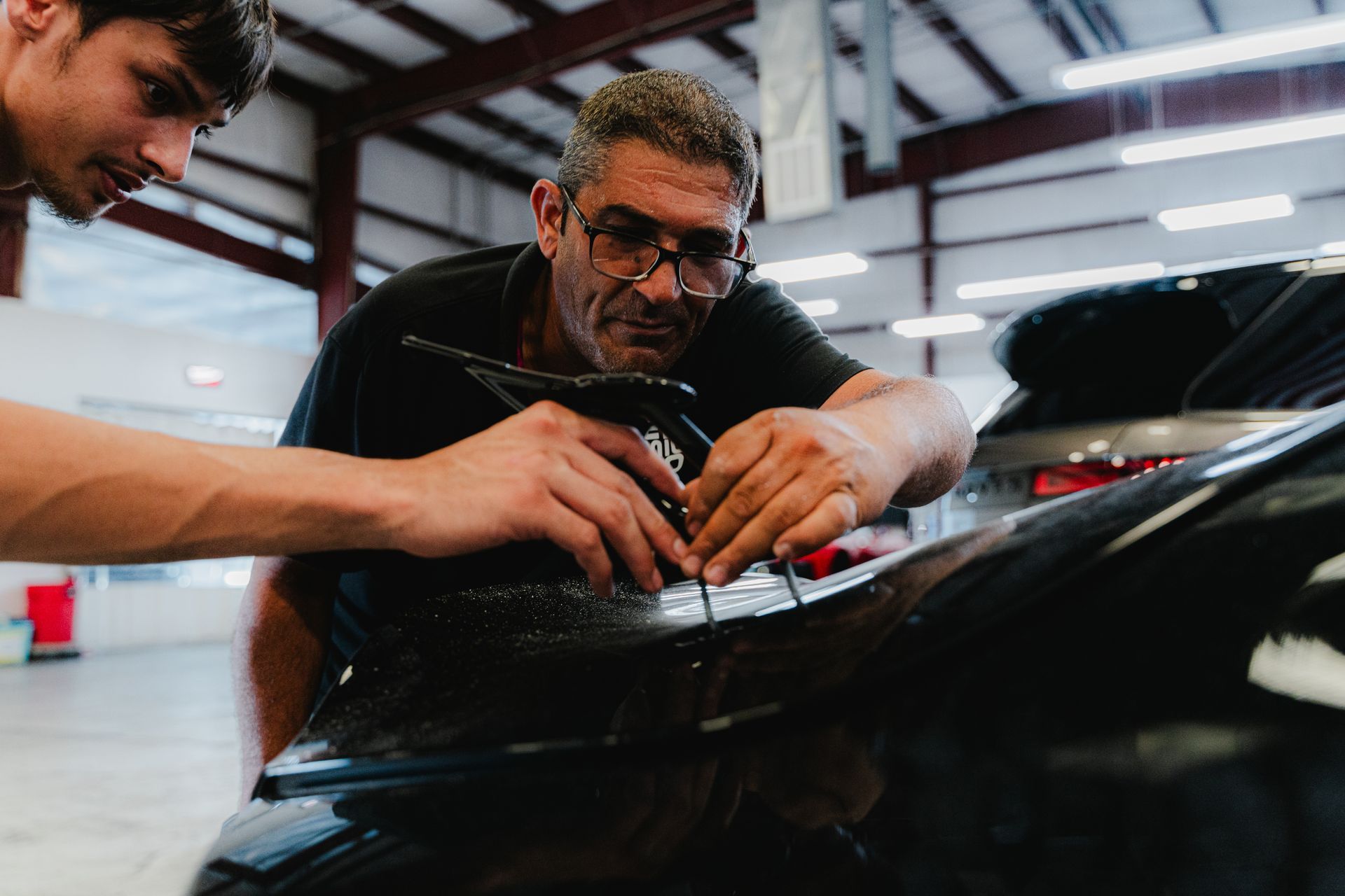 Two people applying film to a black car hood in a workshop