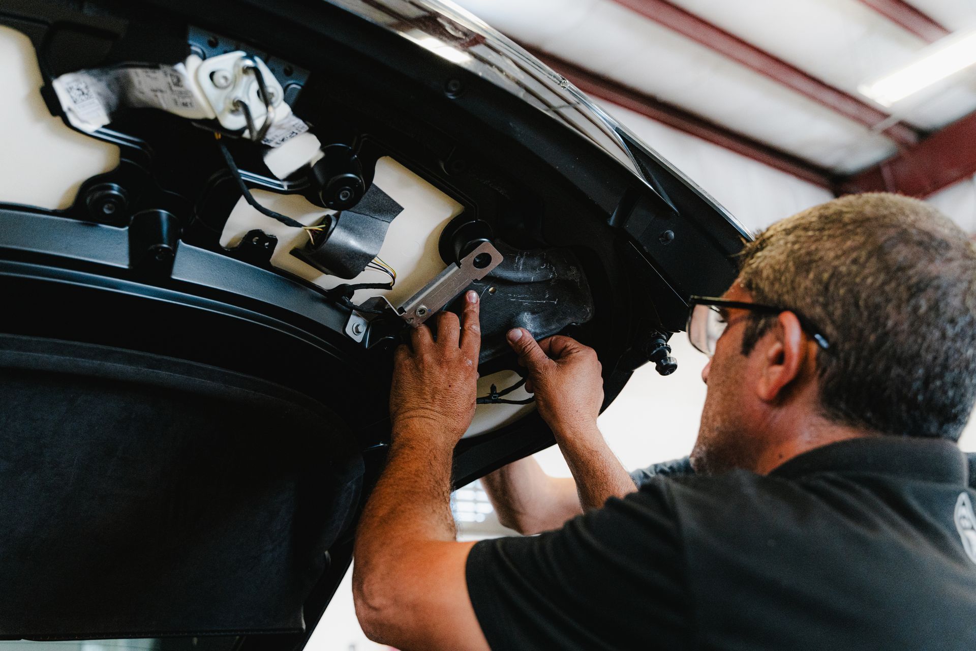 Man working under a car, adjusting components near the front bumper inside a garage