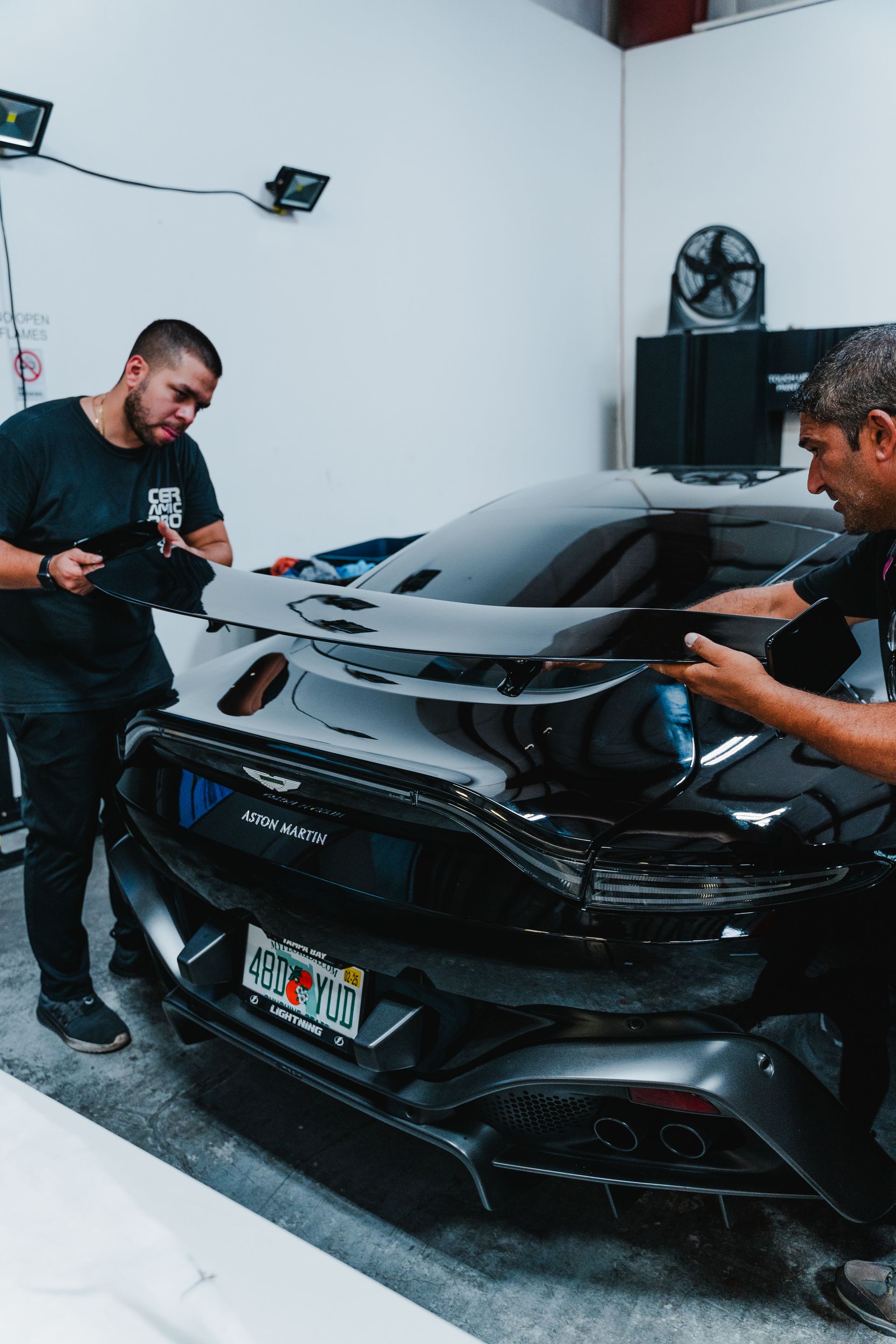 Two people polishing a black sports car in a garage