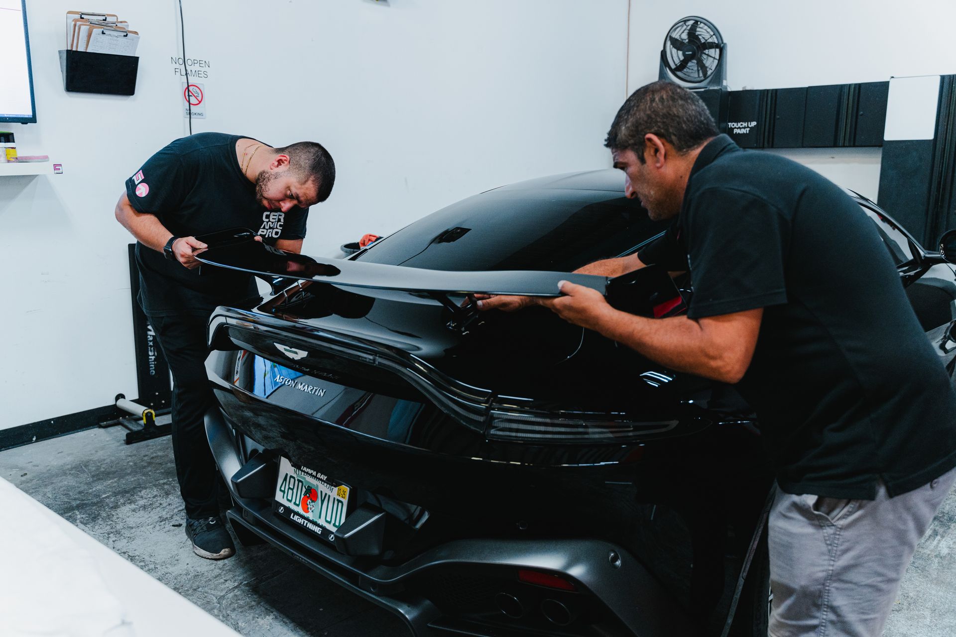 Two mechanics inspecting a black sports car in a garage