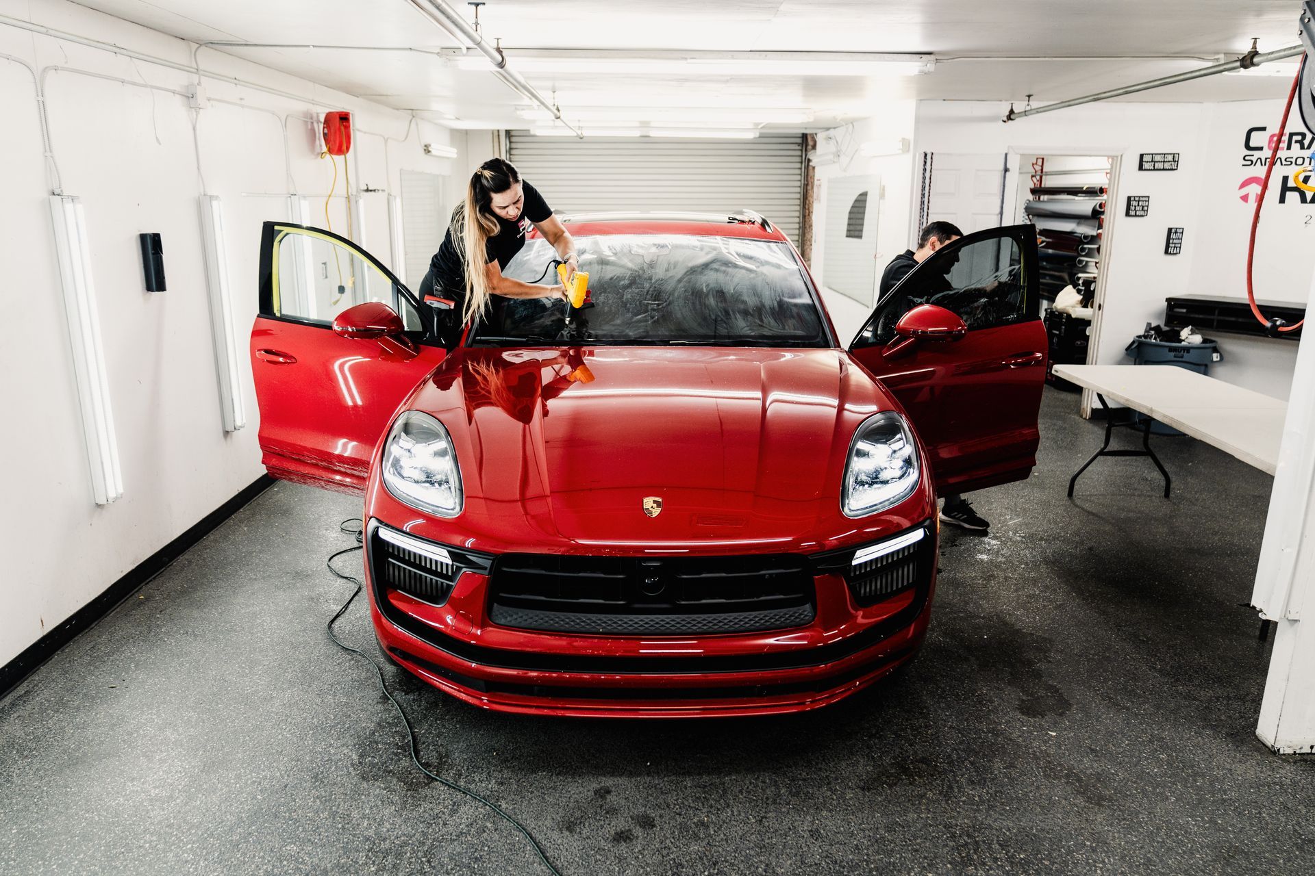 Red sports car in a white garage with both doors open, a person cleaning the windshield.