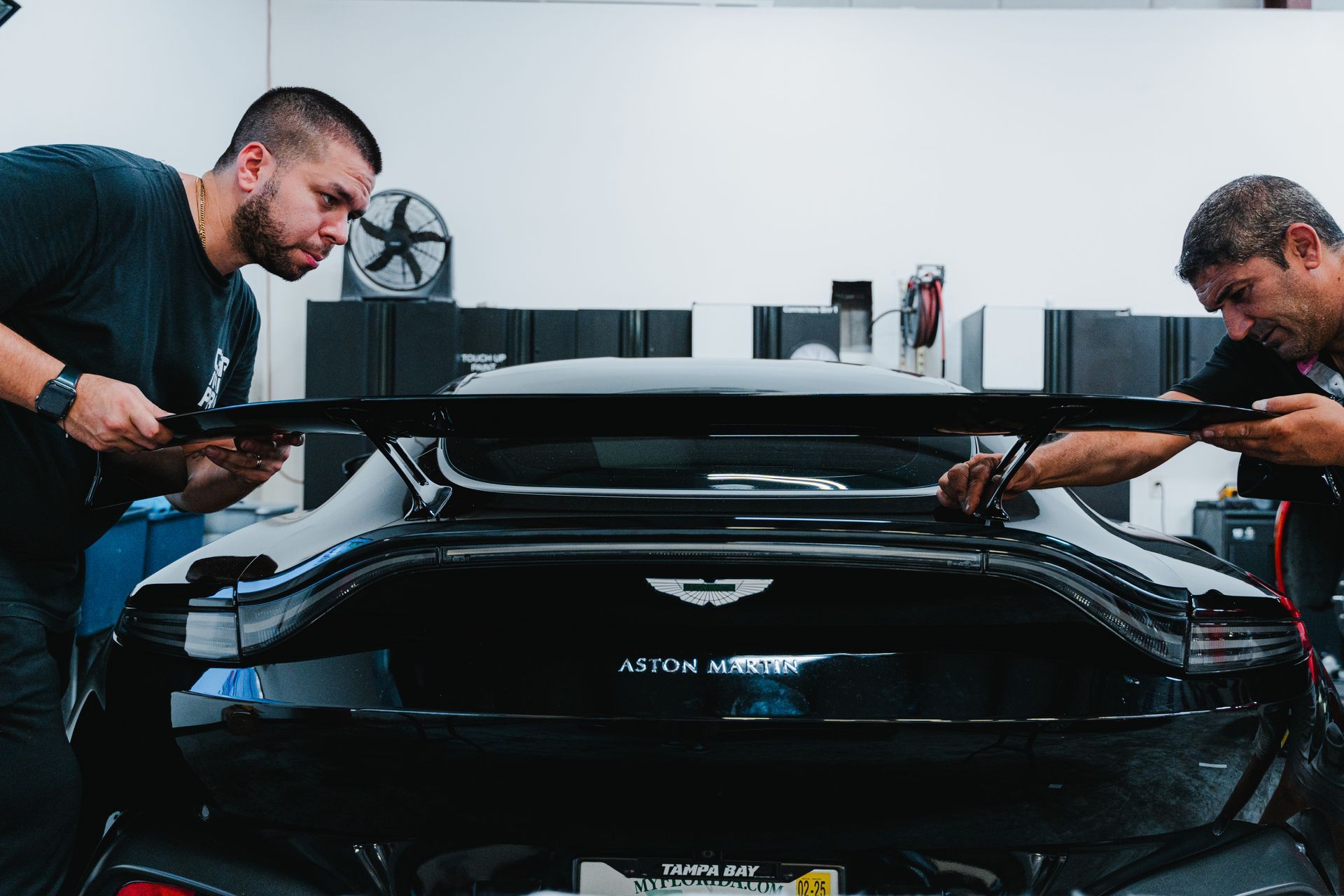 Two mechanics working on a black Aston Martin in a garage