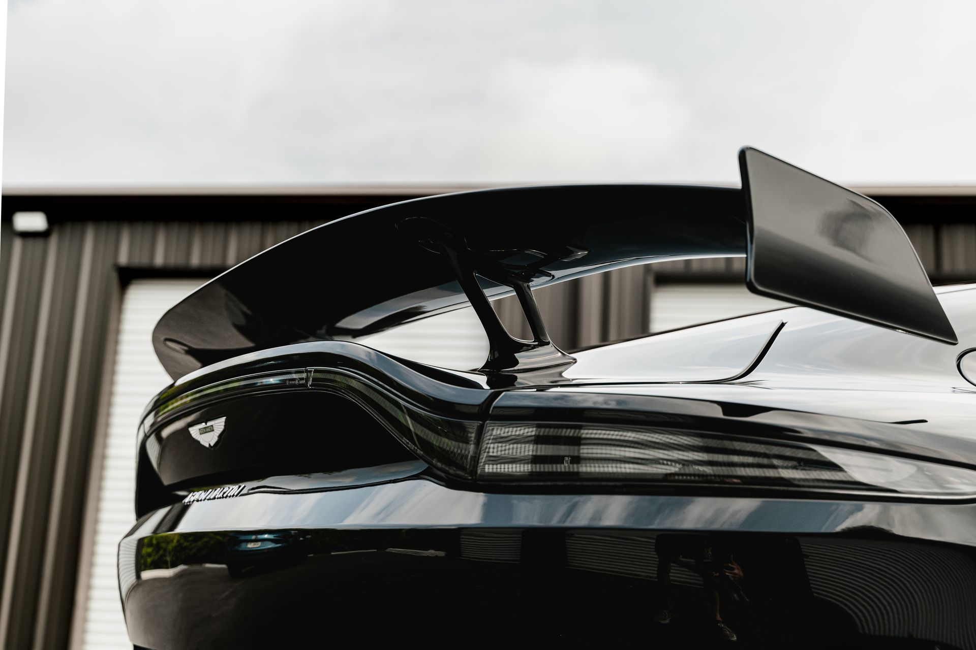 Black sports car with a raised rear wing parked in front of a garage door
