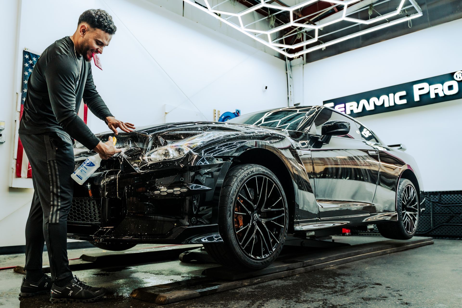 Detailer washing a black sports car in an auto detailing shop