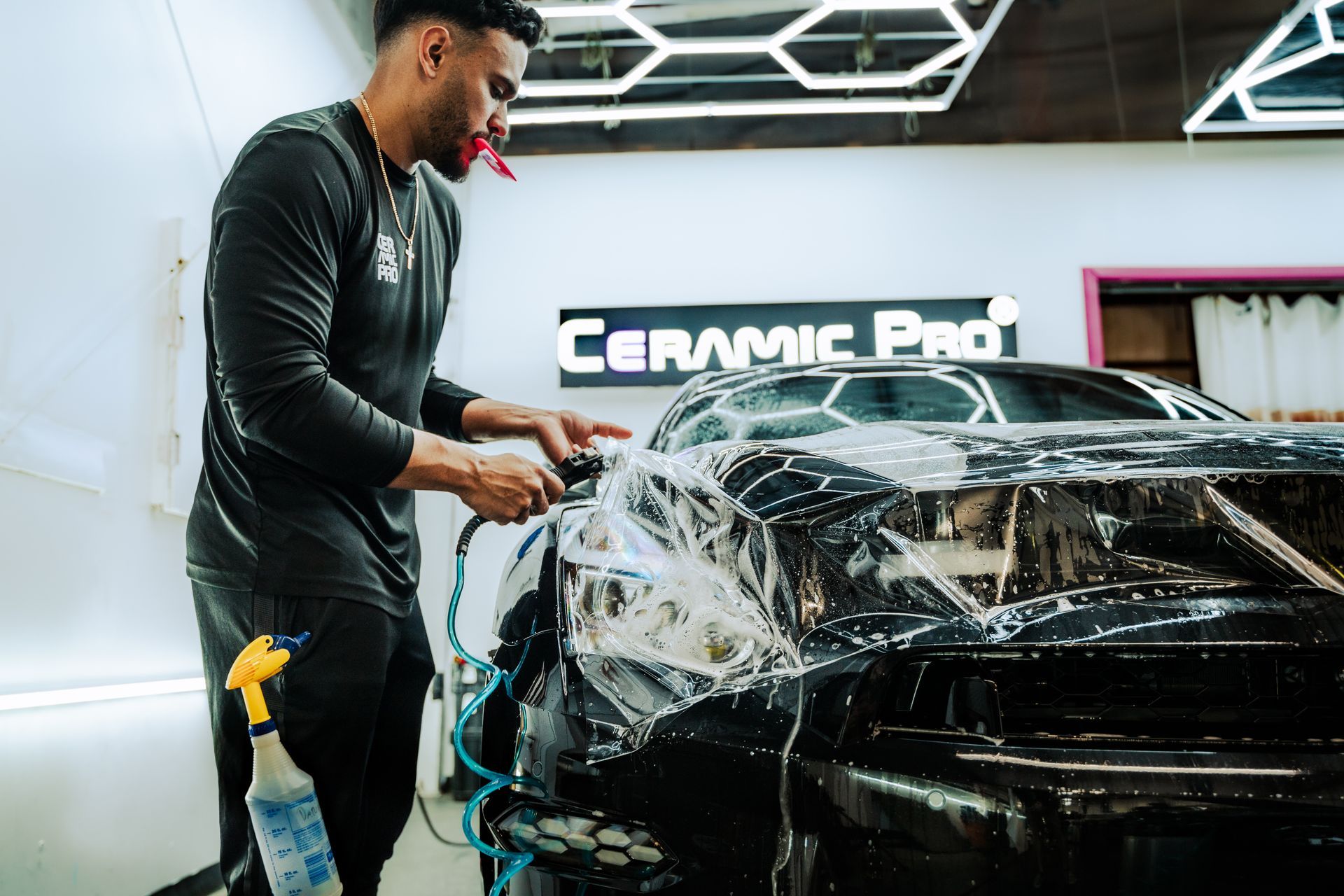 Detailer cleaning a black car with foam in a Ceramic Pro auto shop
