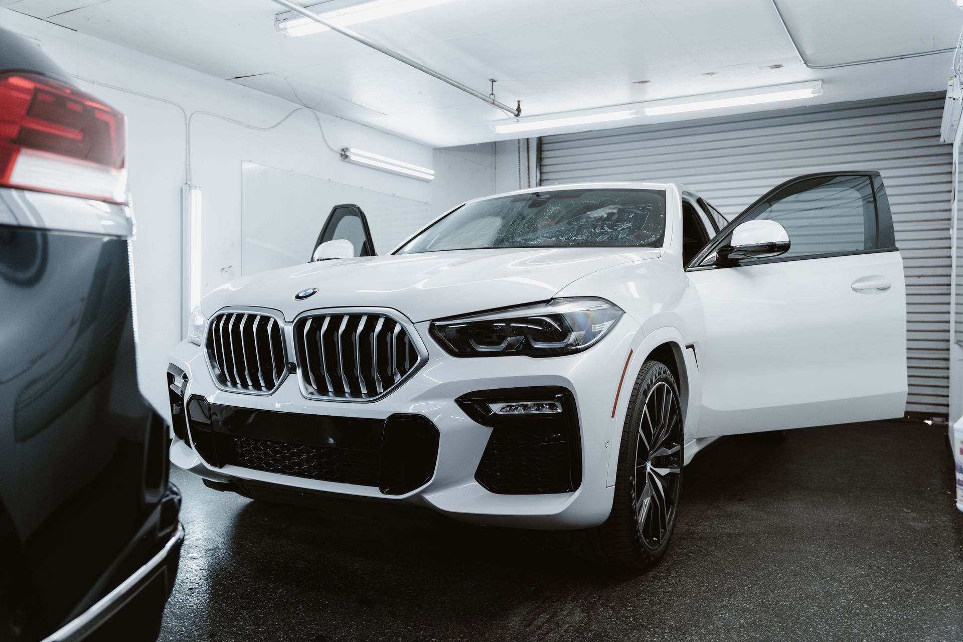 White BMW SUV in a garage with the driver’s door open, viewed from the front-left.
