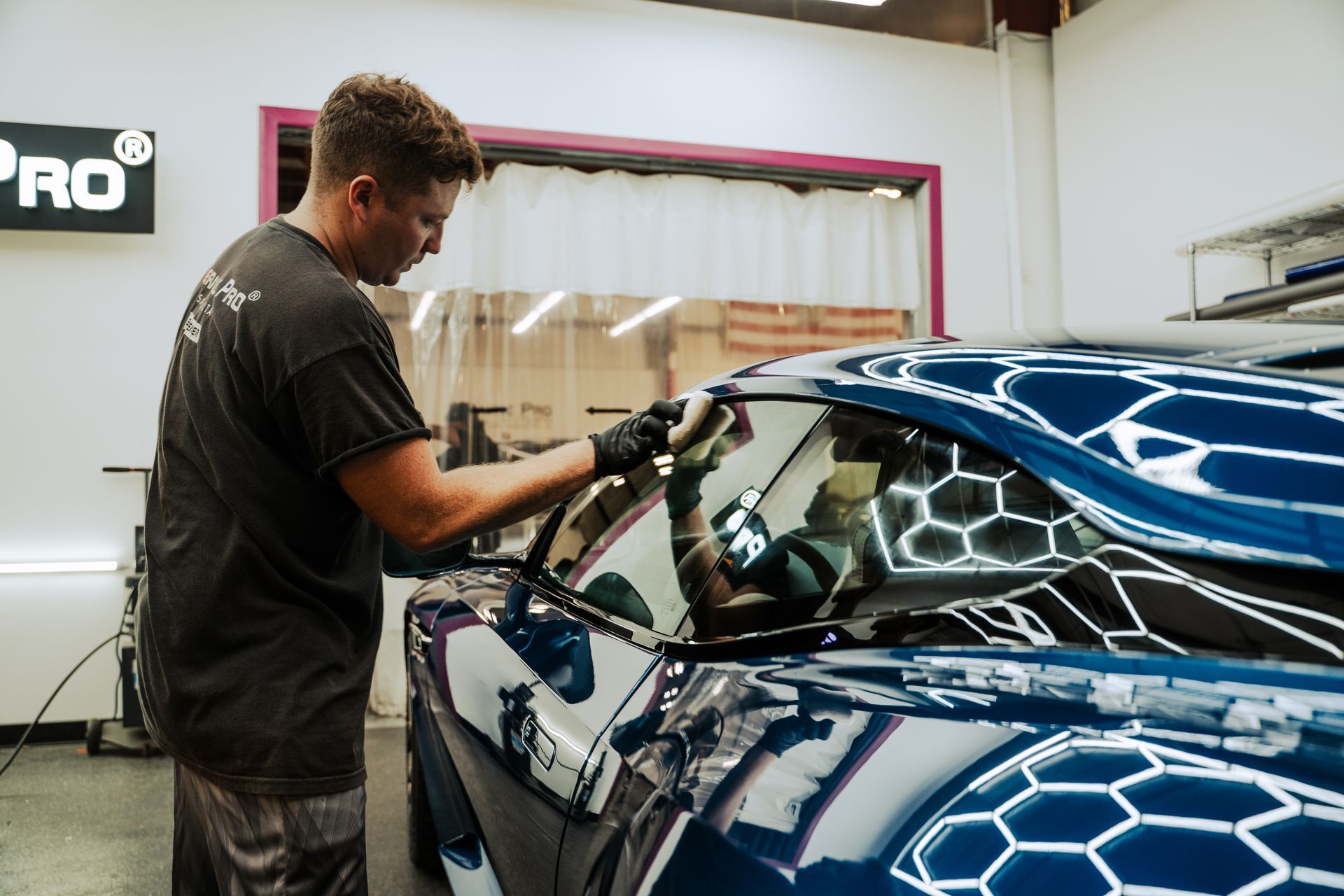Technician applying polish to a blue car in an auto detailing shop