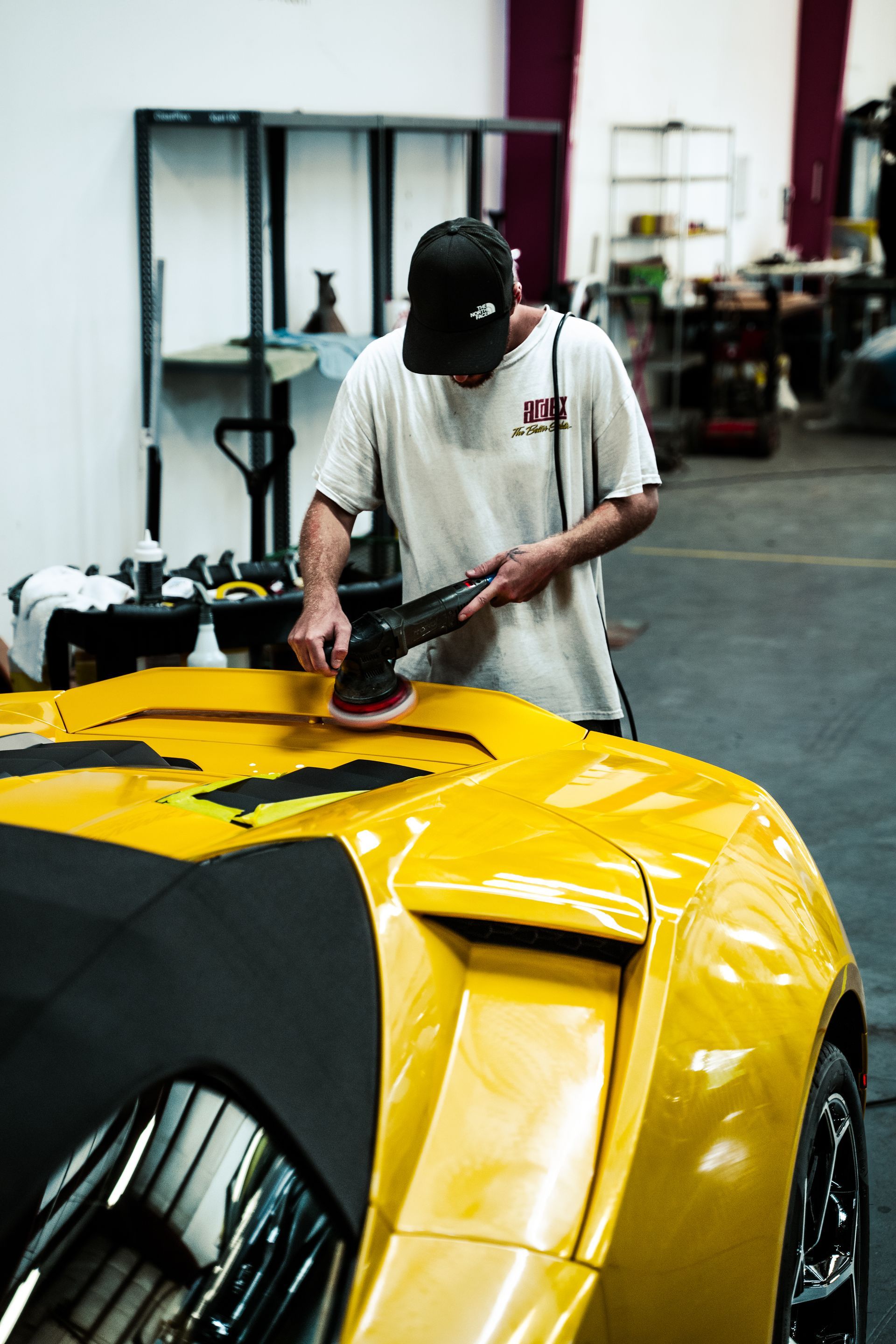 Man polishing a yellow sports car in a garage, focused on the hood.