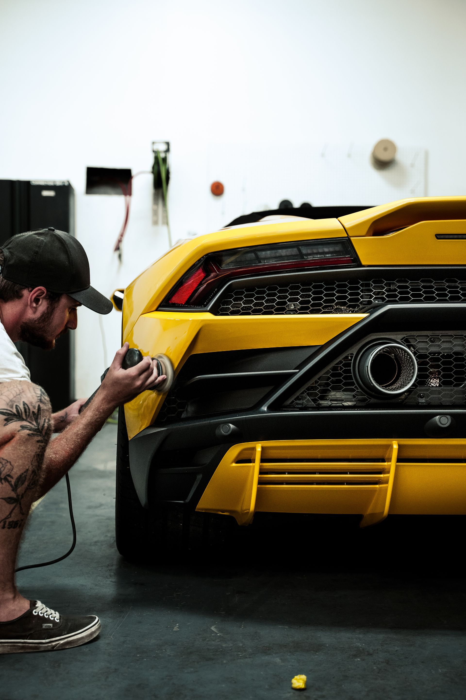 Man polishing the rear of a yellow sports car in a garage