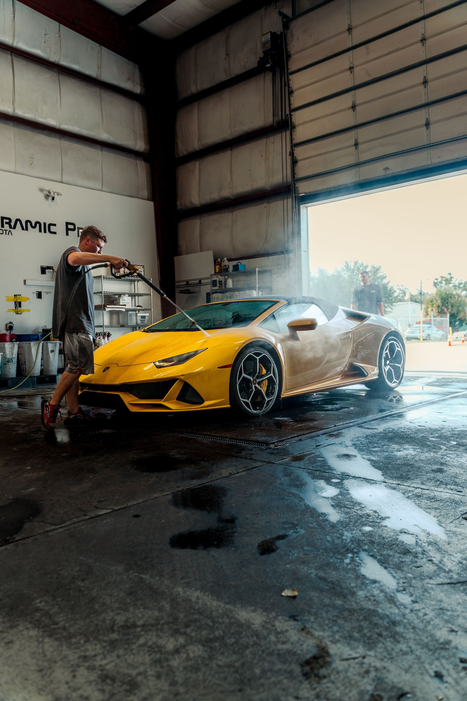 Yellow sports car being washed inside a garage with the door open to daylight.