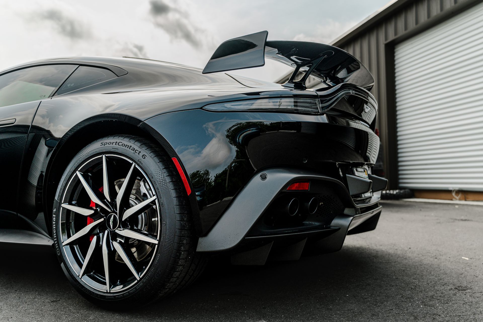 Black sports car with open rear hatch parked outside near a garage door