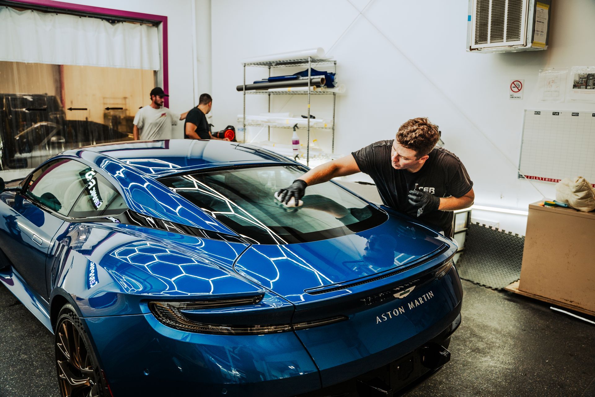 Blue sports car being cleaned in a workshop by a man wiping the windshield