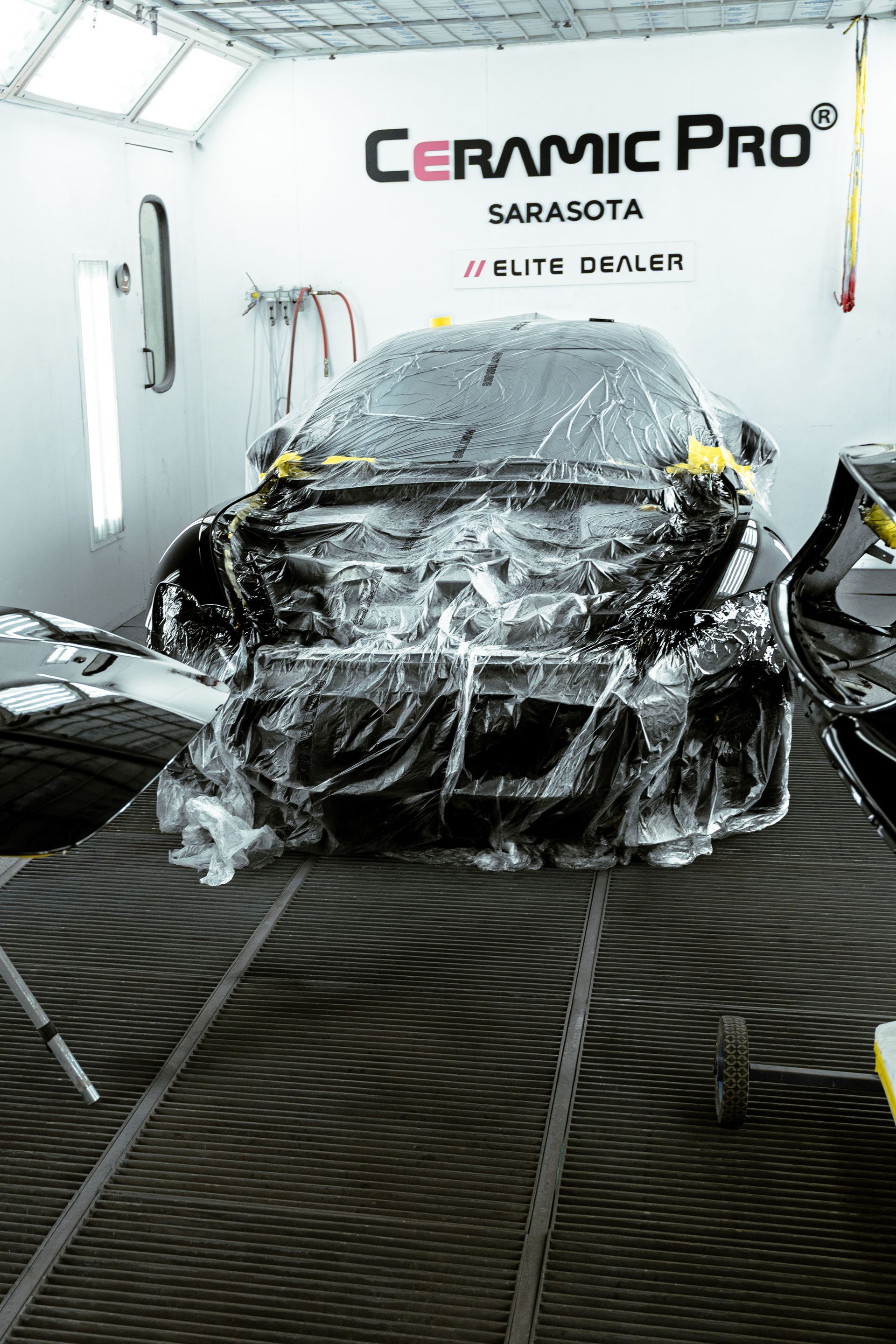 Car being hand-washed under a Ceramic Pro Sarasota sign in a detailing shop