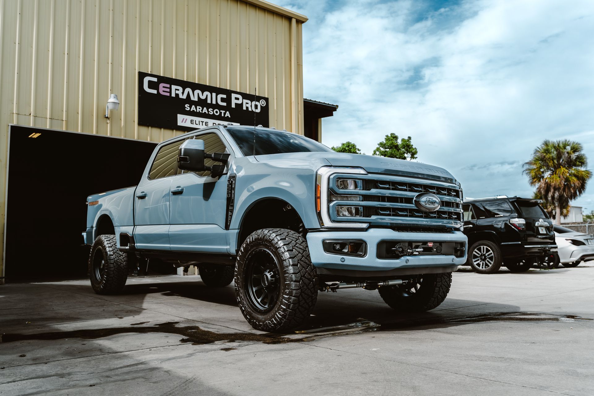 Lifted silver pickup truck outside a Ceramic Pro shop, with another truck in the background