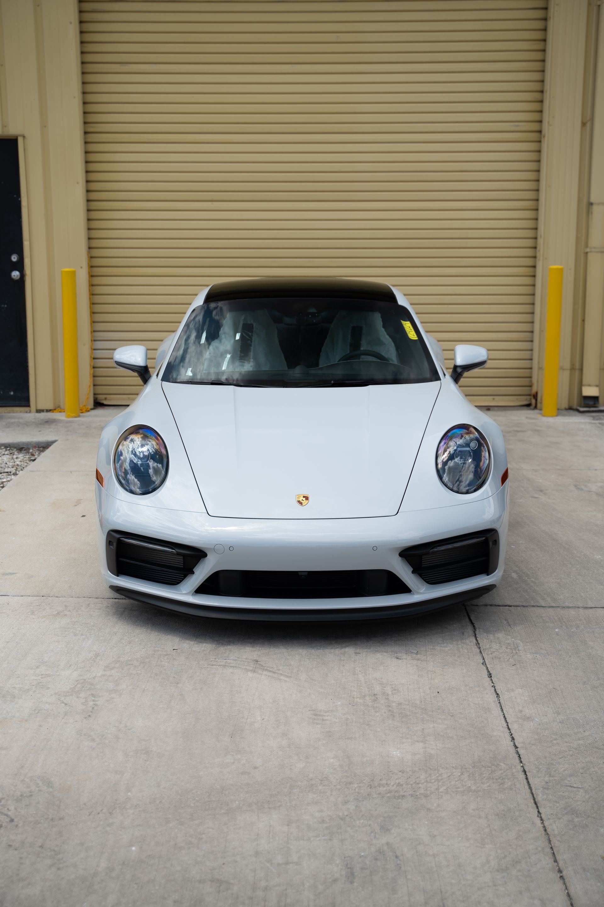 White Porsche 911 parked in front of a closed beige garage door