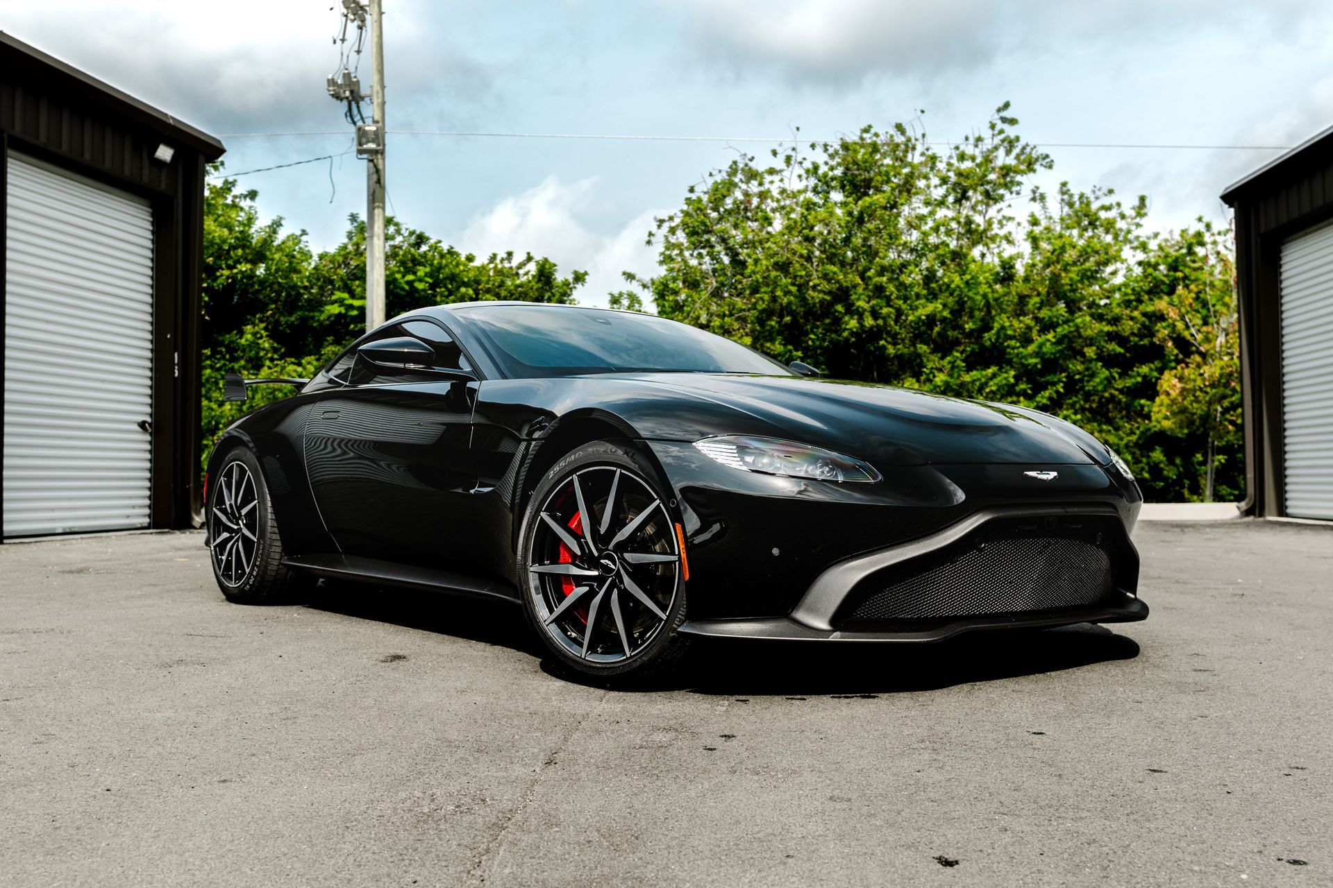 Black sports car parked on pavement between garages, viewed from the front-left.