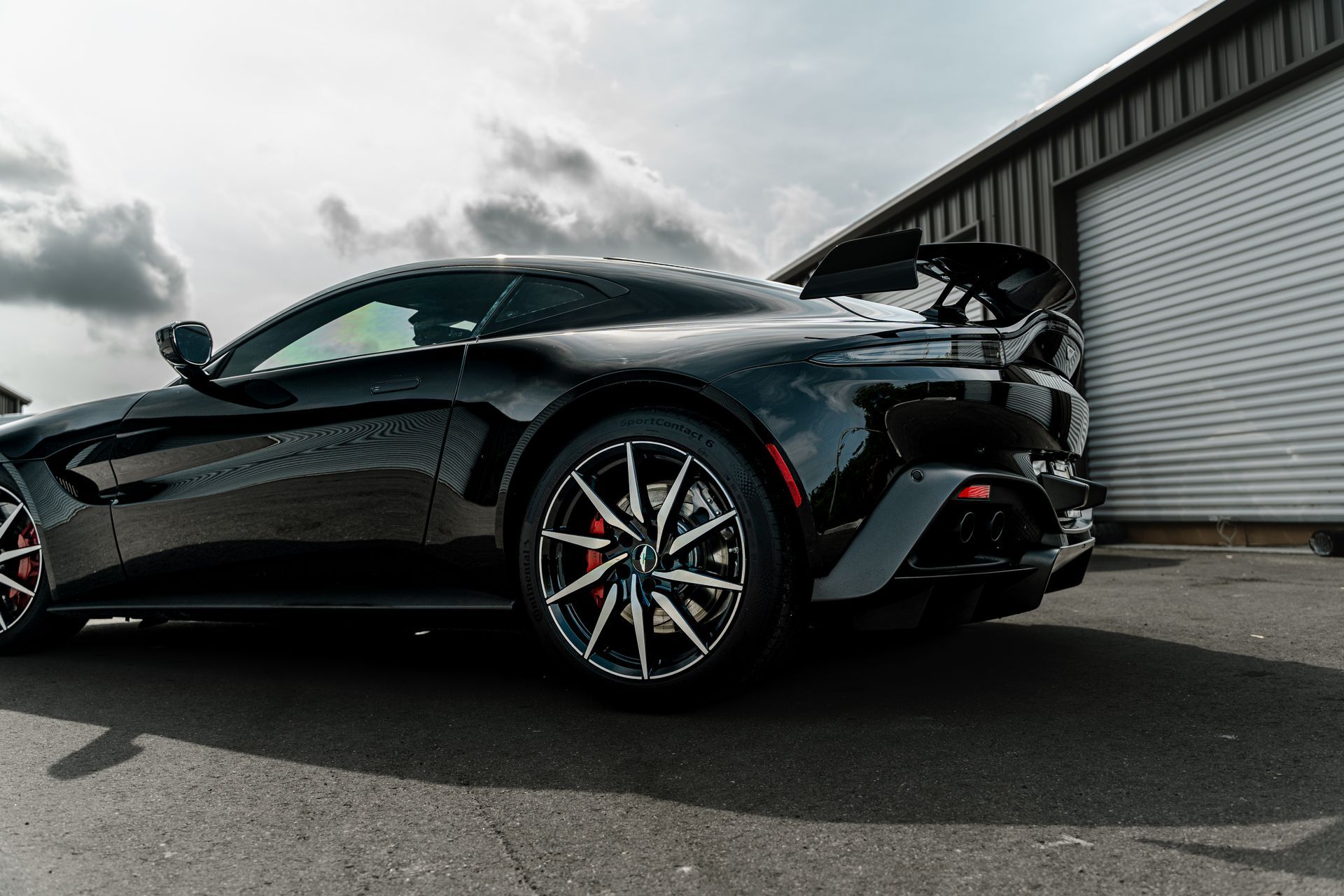 Black sports car parked beside a corrugated metal building under cloudy skies