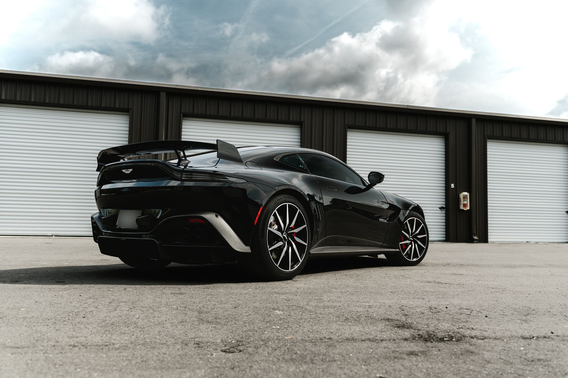 Black sports car parked on pavement in front of white garage doors under cloudy sky