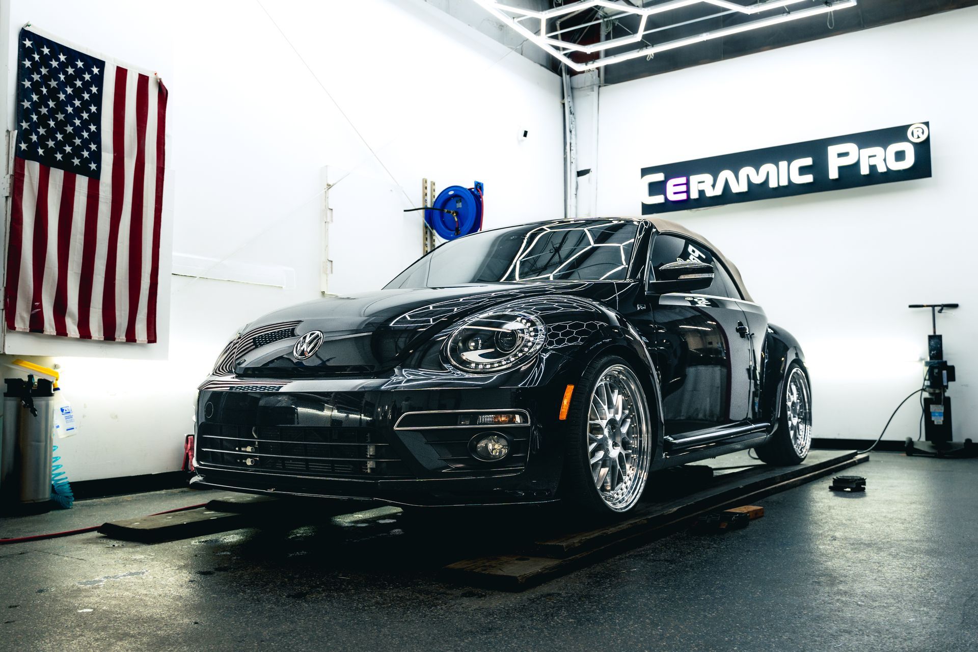 Black sports car in a detailing shop with an American flag and Ceramic Pro sign.
