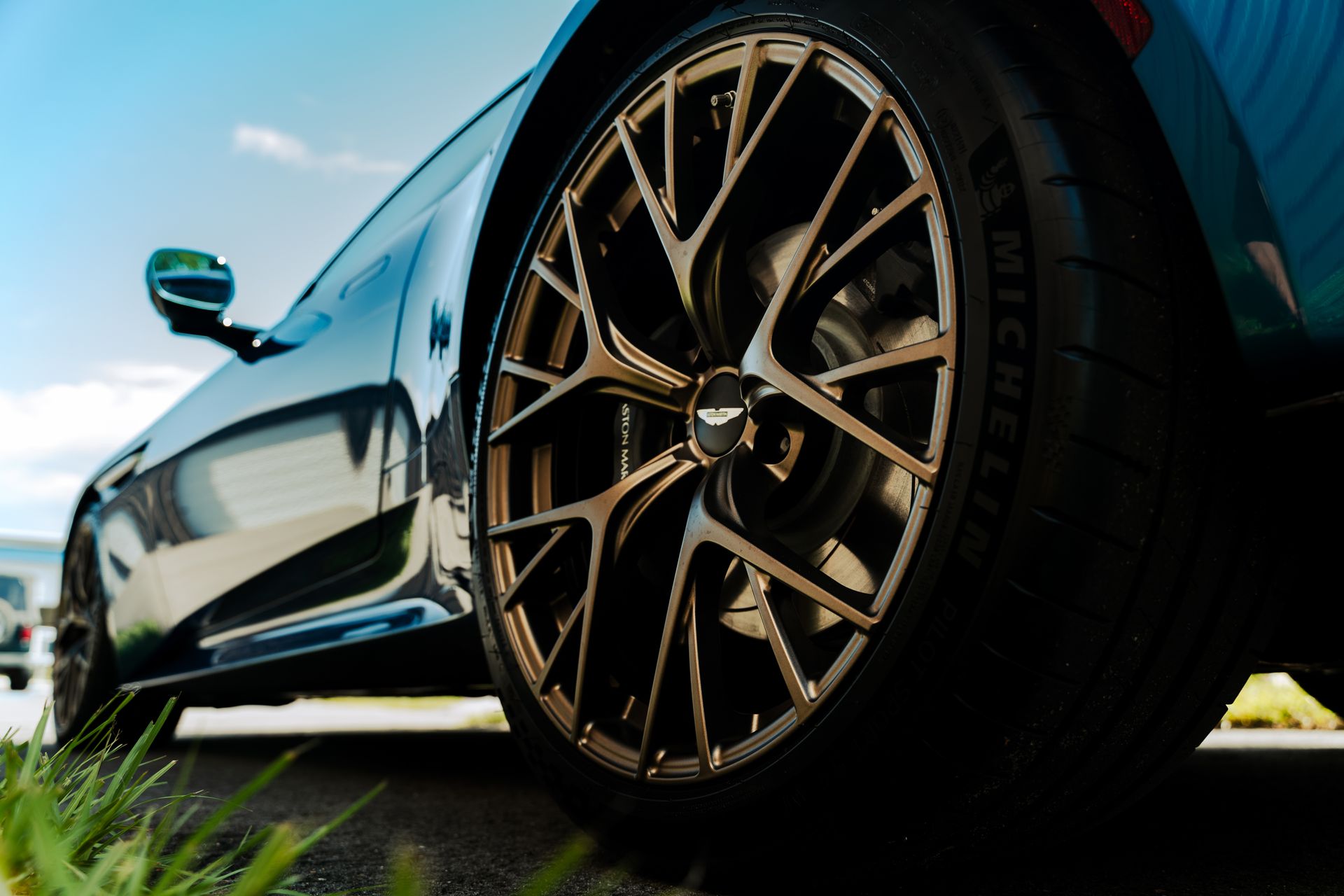 Low-angle view of a black sports car with large bronze alloy wheel on grass