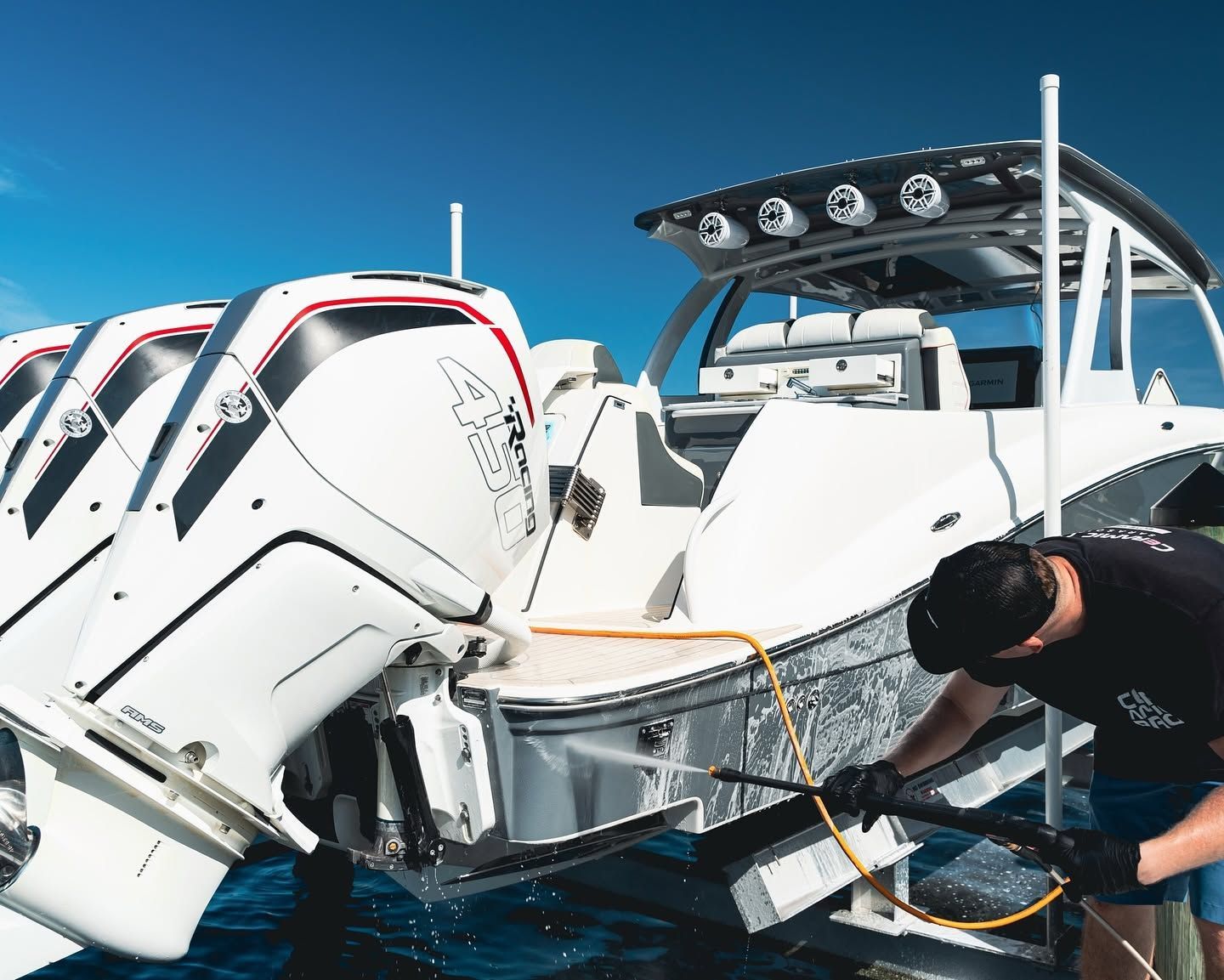 Person cleaning a white speedboat at a marina, with another boat beside it under a blue sky