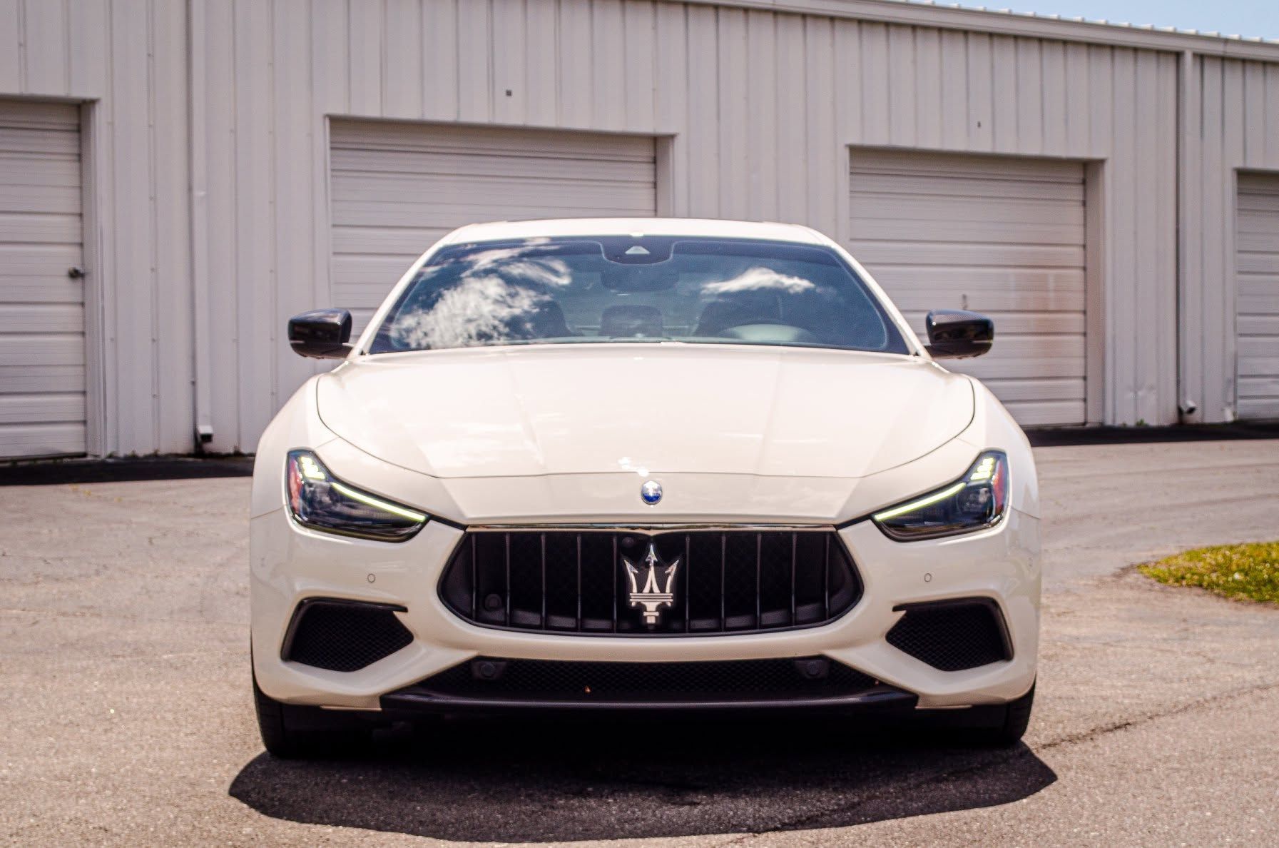 White Maserati parked in front of garage doors on a paved lot