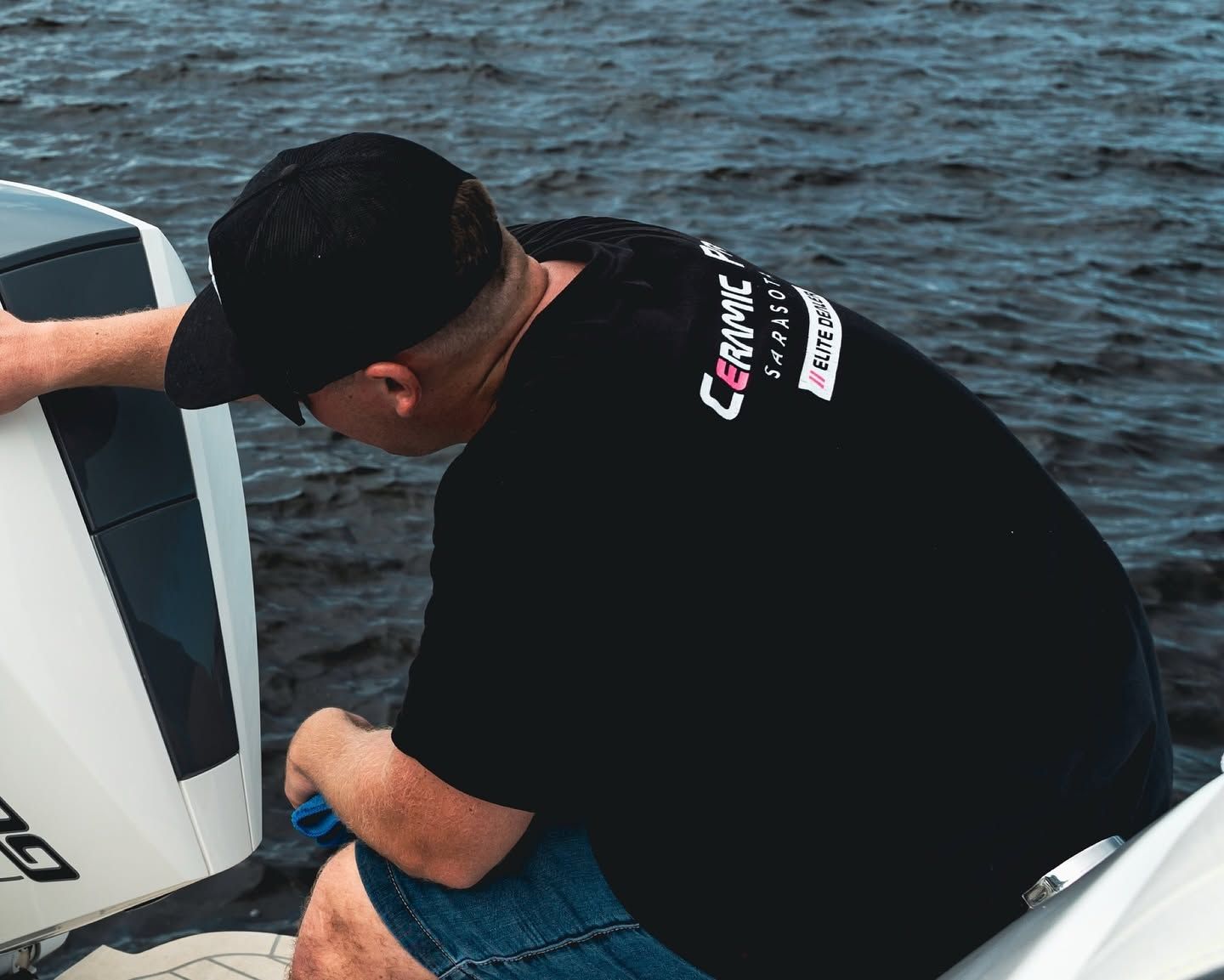 Person in a black shirt and cap leaning into a boat on the water