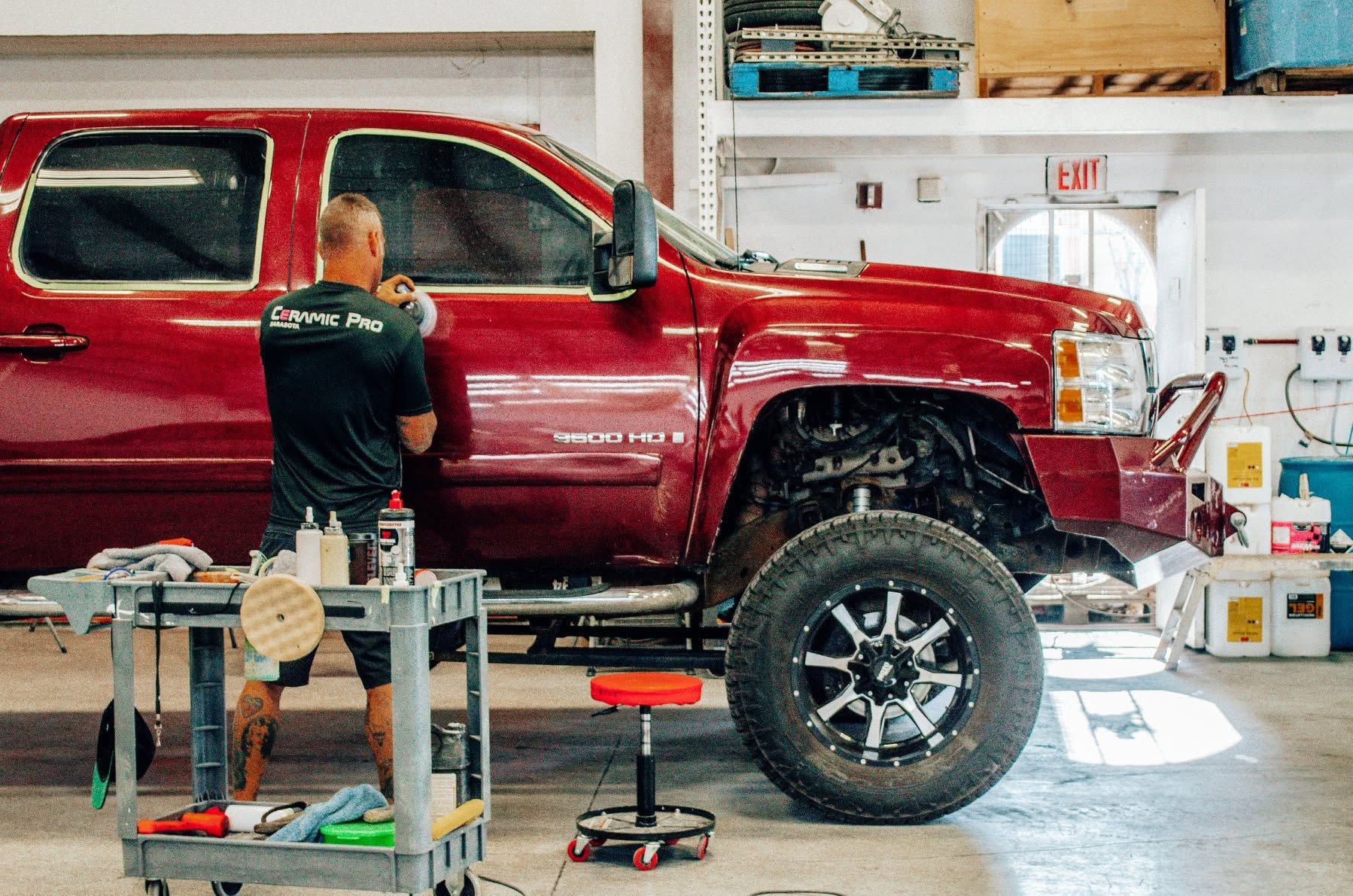 Red pickup truck in a garage with a mechanic working beside it on a lift