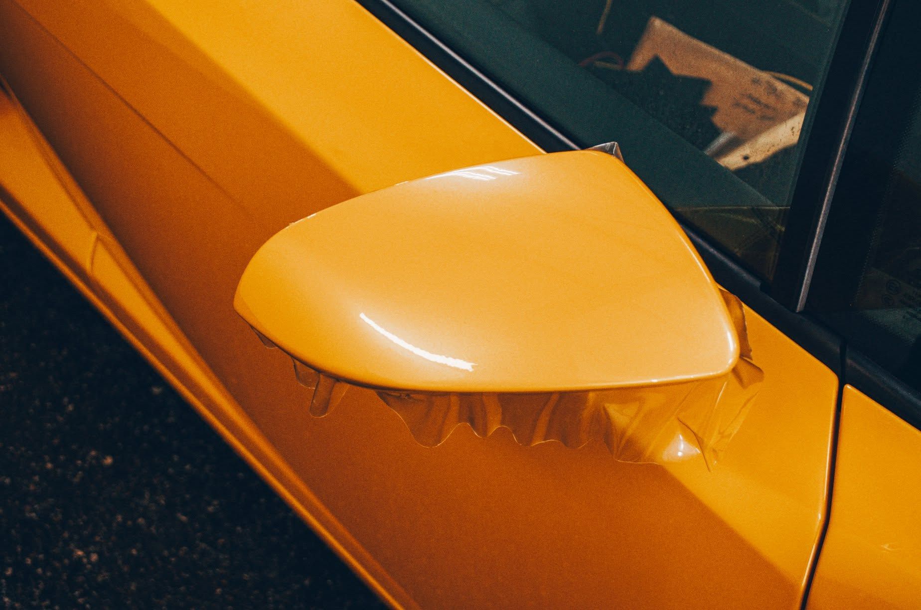 Close-up of a yellow car’s side mirror and door, with the mirror folded outward.