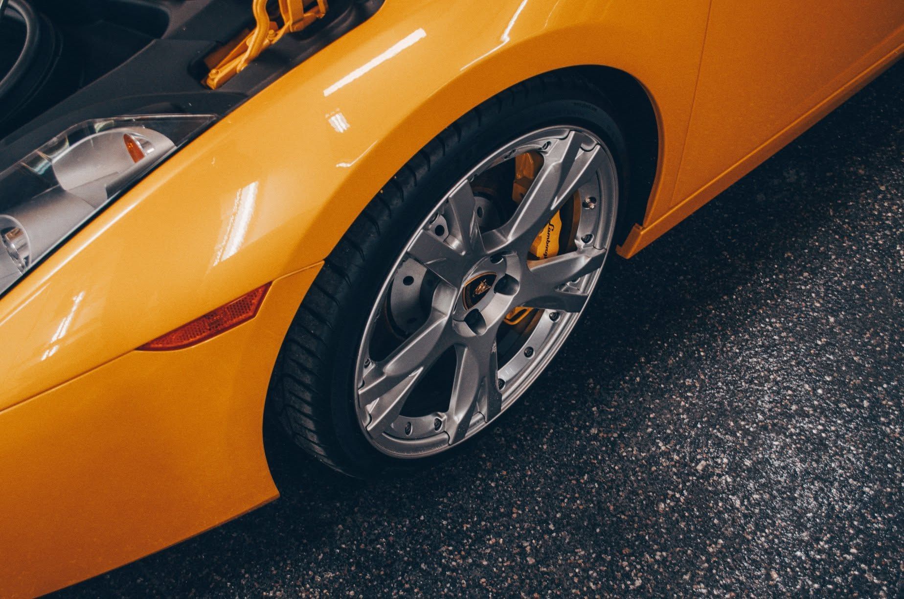 Close-up of an orange sports car wheel and fender on a dark showroom floor