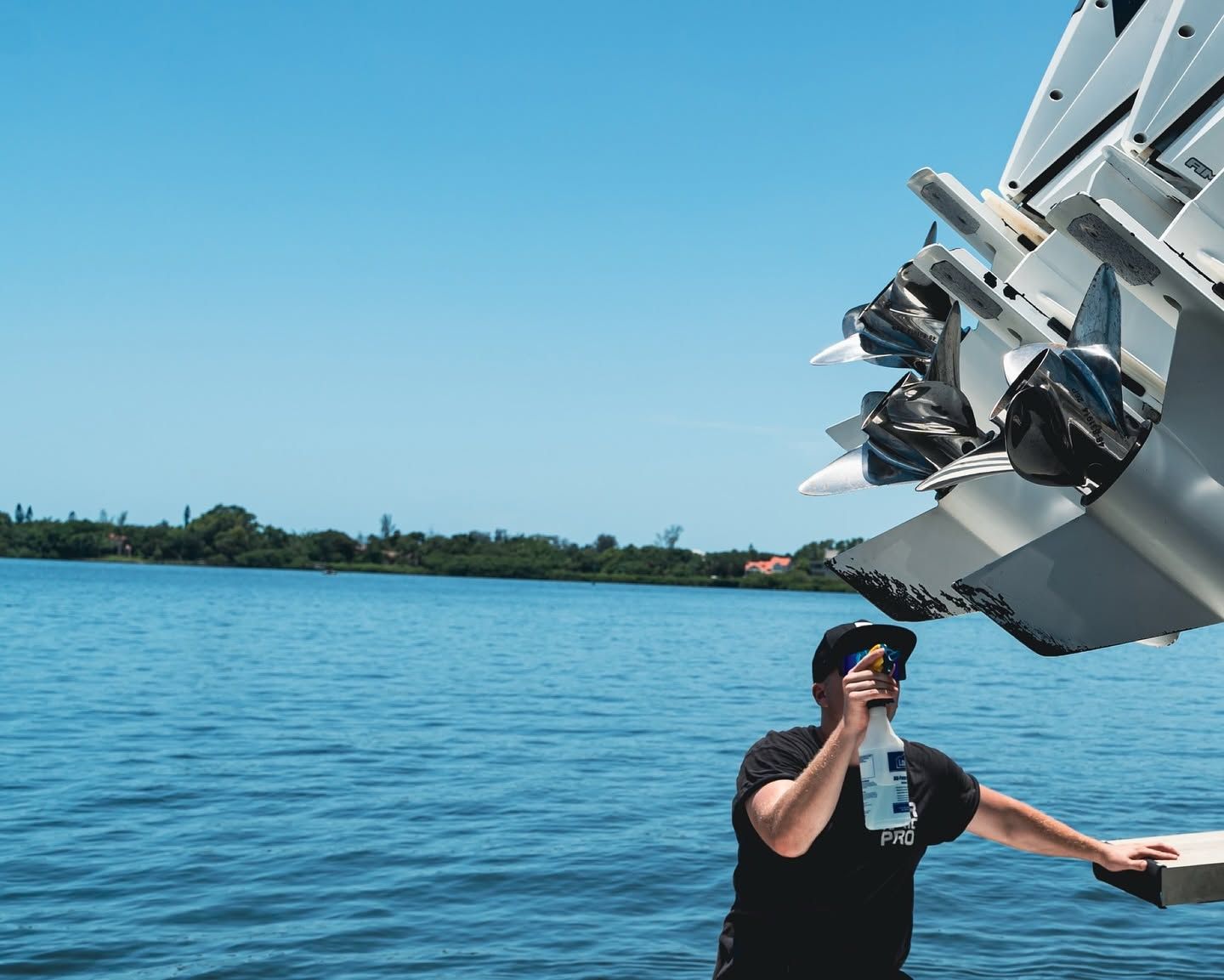 Man in black shirt reaching toward a boat propeller over blue water under a clear sky